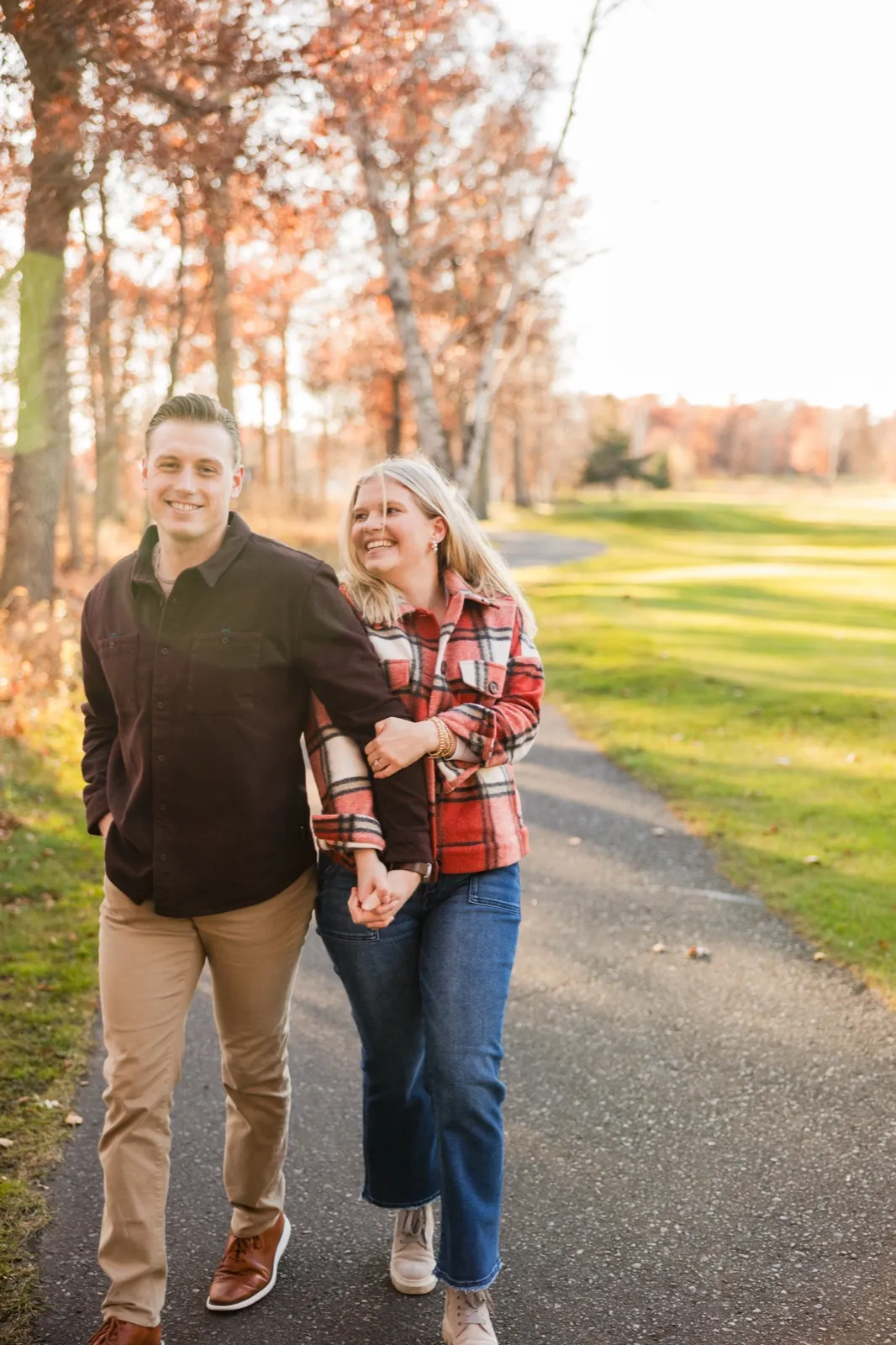 Maddy and Tyler walk hand in hand down a cart path lined with autumn trees — Tim Larsen Photography, Brainerd Lakes MN