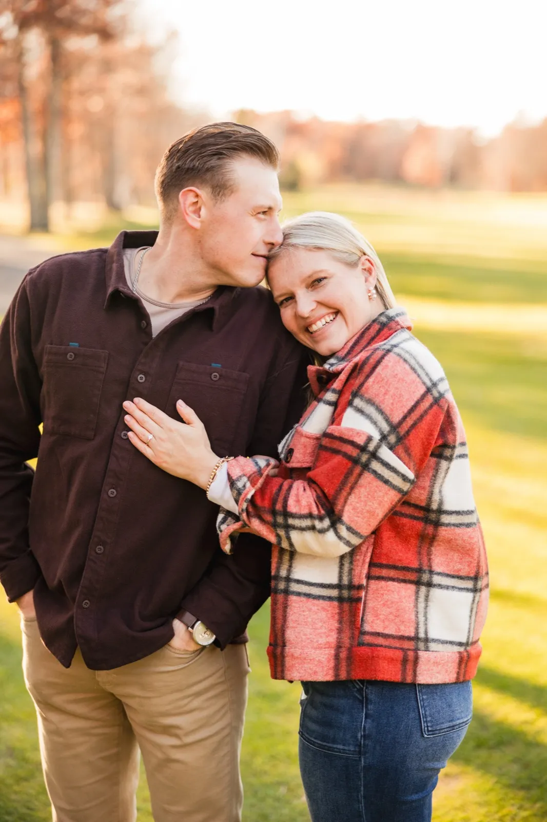 Tyler rests his face against Maddy's temple as she smiles at the camera on the open grass — Tim Larsen Photography, Brainerd Lakes MN