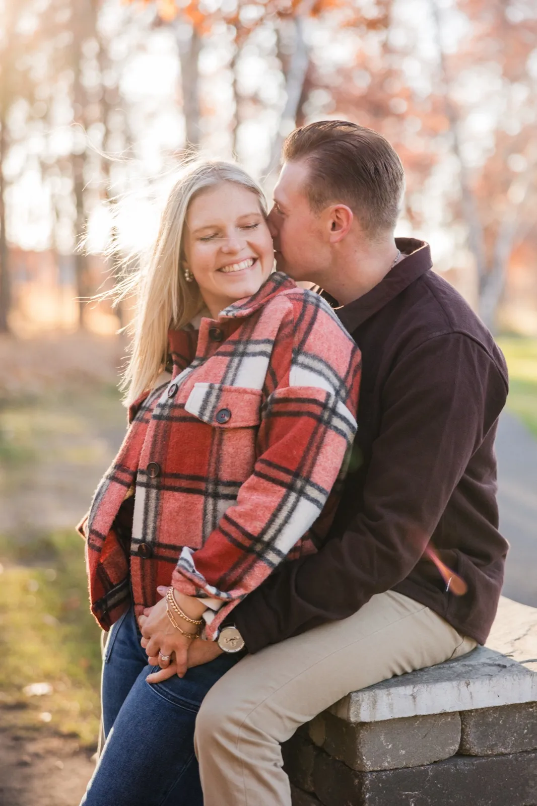 Tyler kisses Maddy's cheek as they sit on a low stone wall at Grand View Lodge