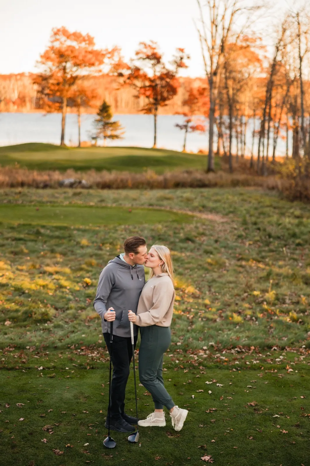Maddy and Tyler kiss on the course with the lake and peak fall color behind them — Tim Larsen Photography, Brainerd Lakes MN