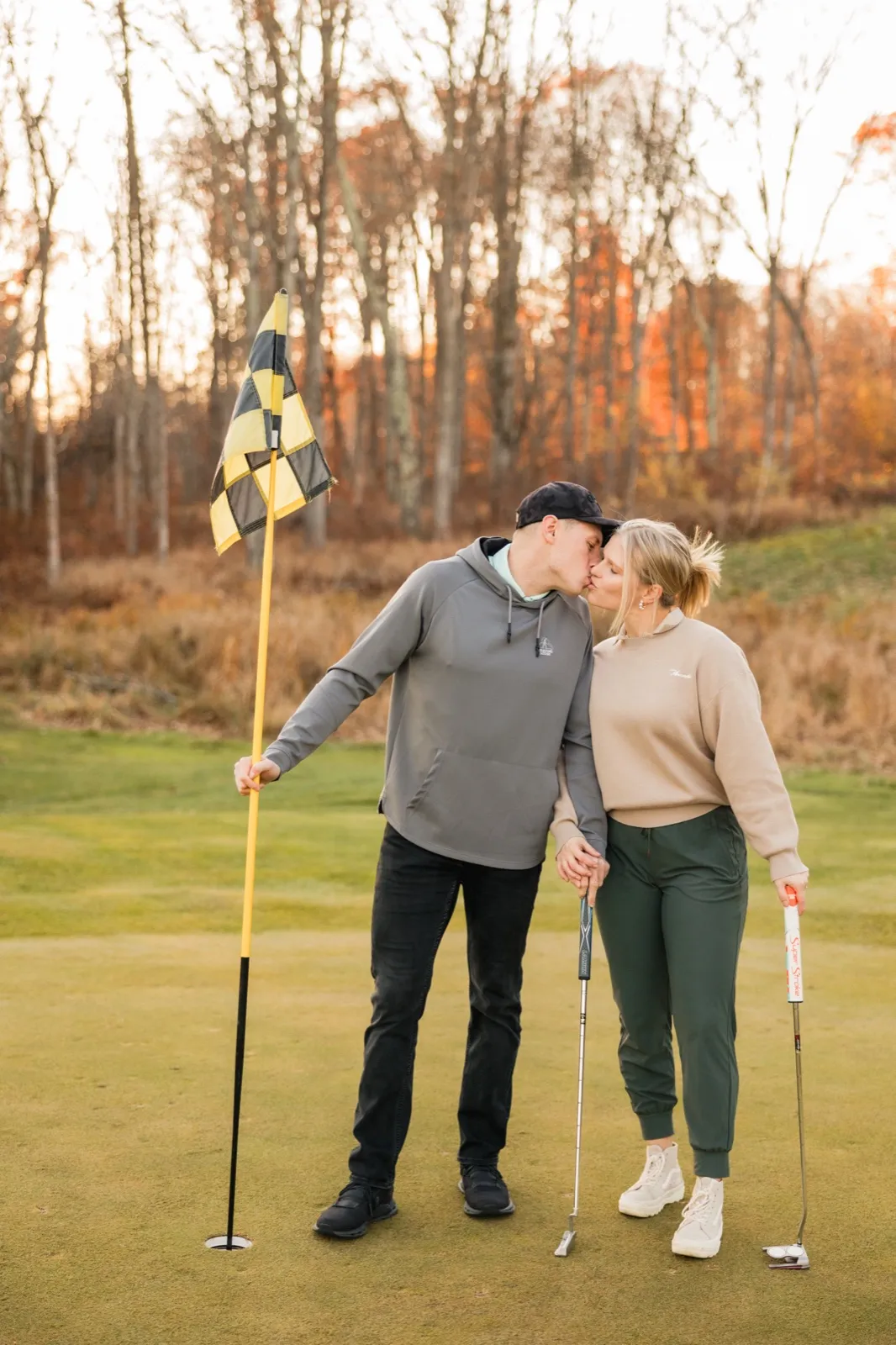 Tyler holds the checkered flag as he and Maddy kiss on a putting green — Tim Larsen Photography, Brainerd Lakes MN