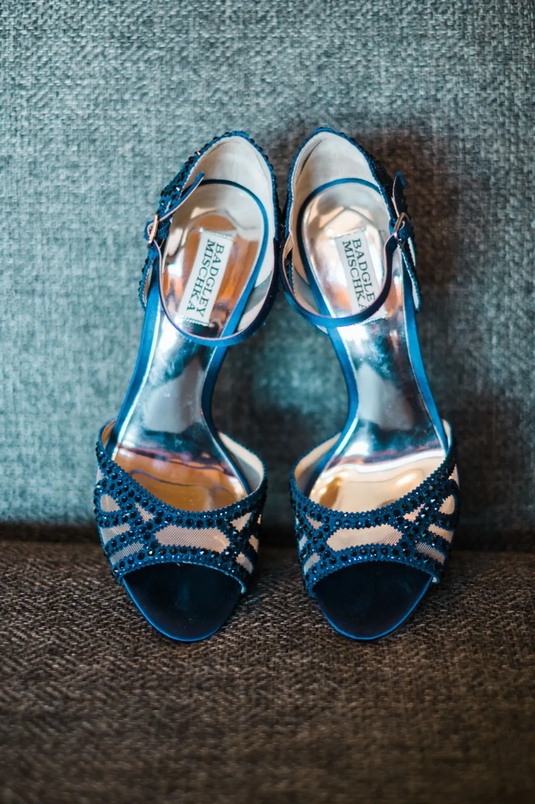 Navy blue beaded peep-toe wedding heels rest on a textured gray chair.