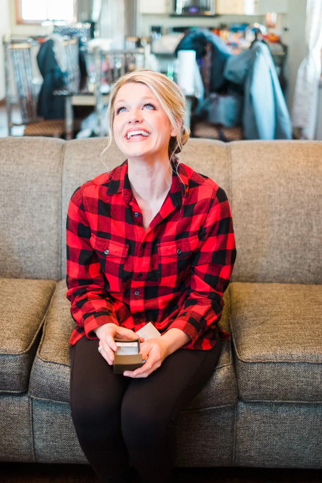 Morgan laughs on the couch with a small gift box in her lap while getting ready for her Breezy Point wedding