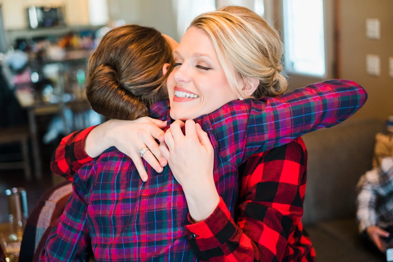 Morgan closes her eyes and smiles while hugging a bridesmaid in a purple plaid shirt.