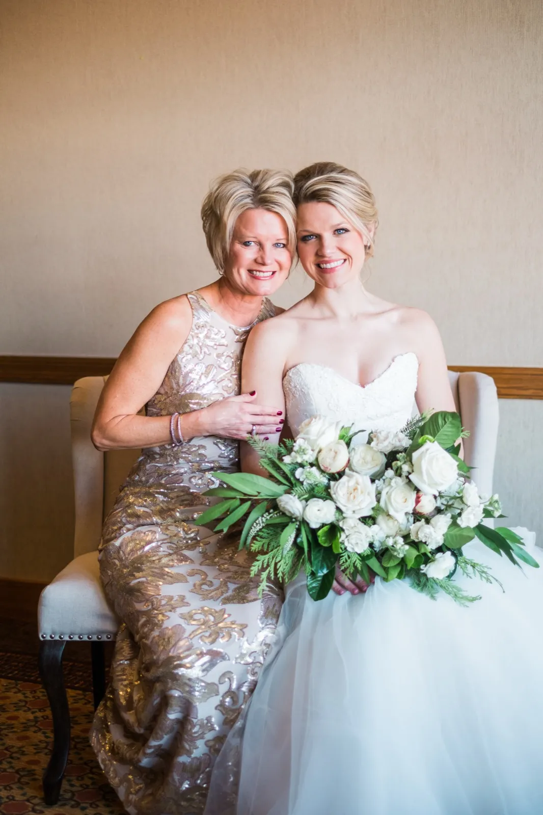 Morgan and her mother sit together for a portrait, with a white bouquet and greenery across Morgan’s lap.