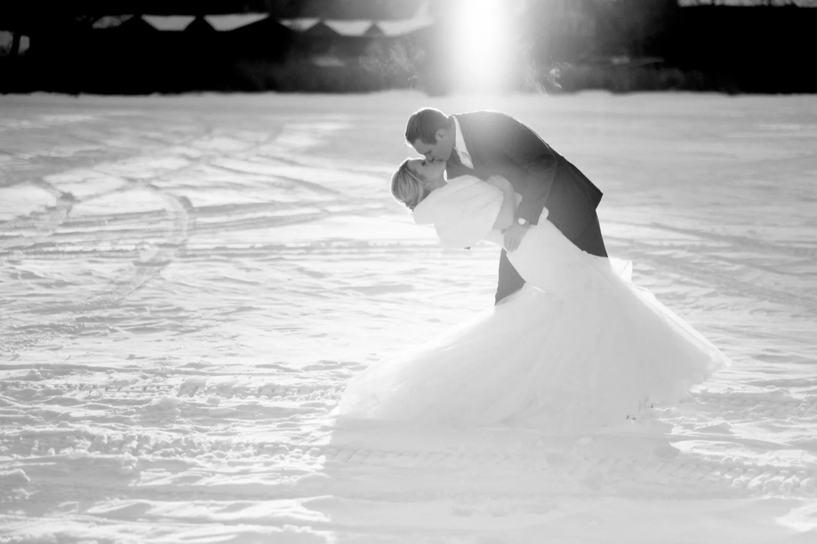 Cole dips Morgan for a kiss on the snowy lake as low sunlight catches their breath, photographed in black and white.