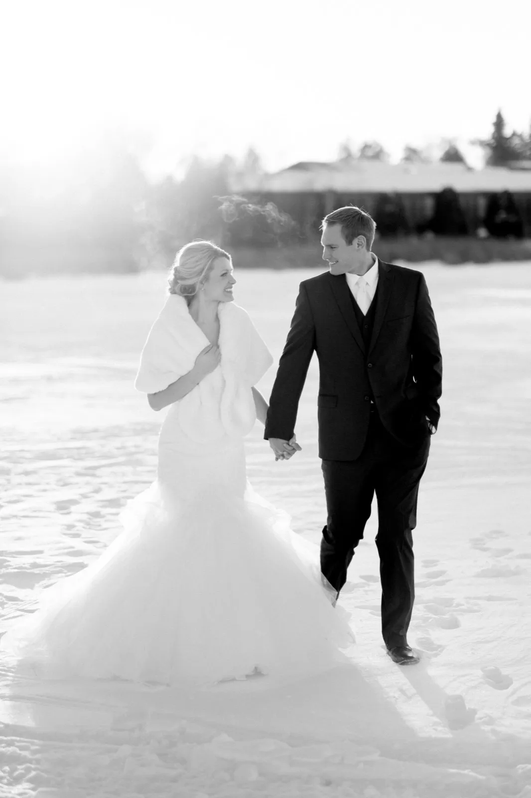 Morgan and Cole walk hand in hand on snow-covered Pelican Lake with their breath visible in the winter light