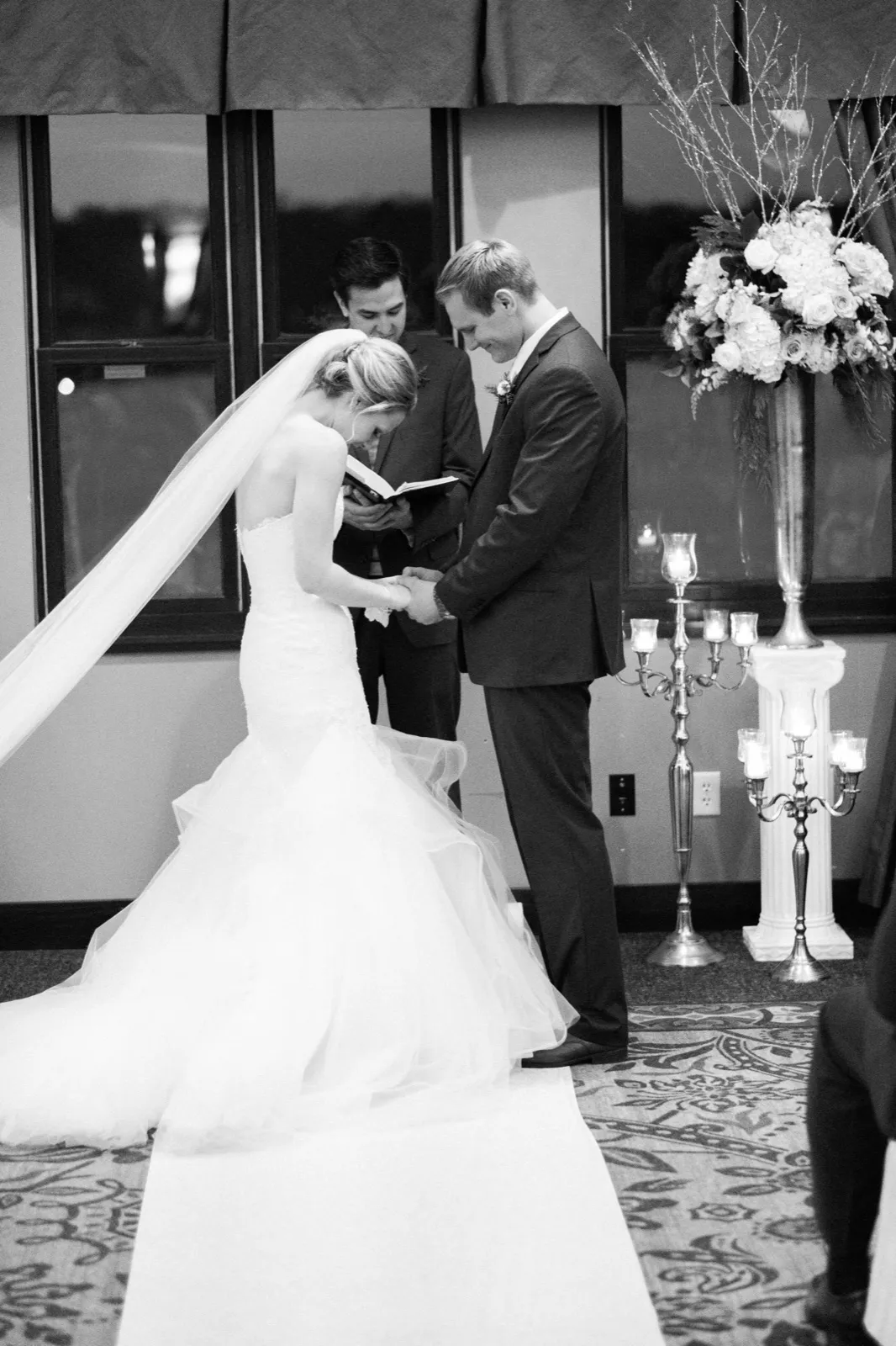Morgan and Cole bow their heads as the officiant reads, with her long veil and train spread behind her.