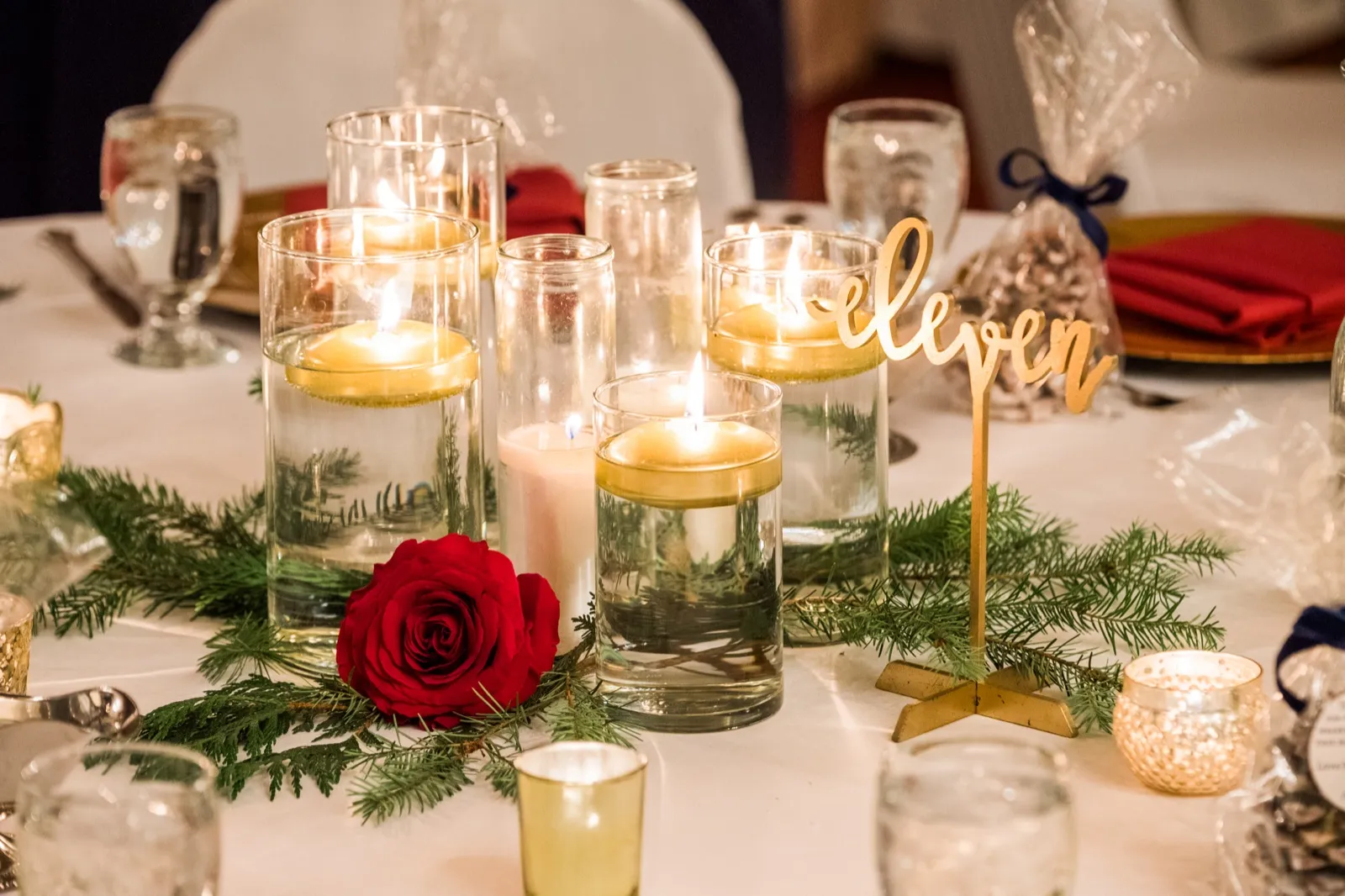 Floating candles, a red rose, greenery, and a gold table number eleven decorate a reception table.
