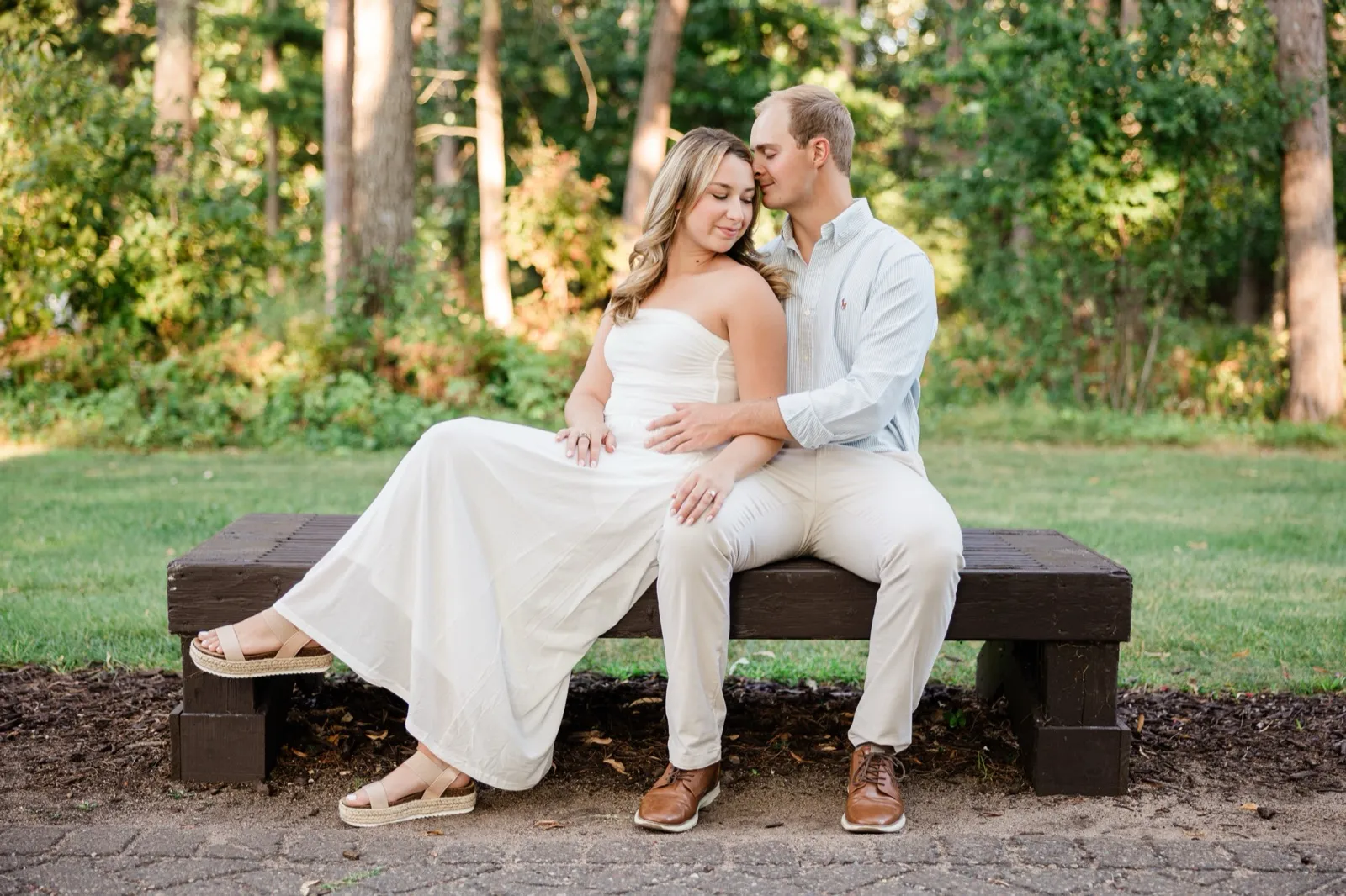 Olivia and Adam sit close on a wooden bench at the pine forest edge, Adam kissing her temple — Tim Larsen Photography