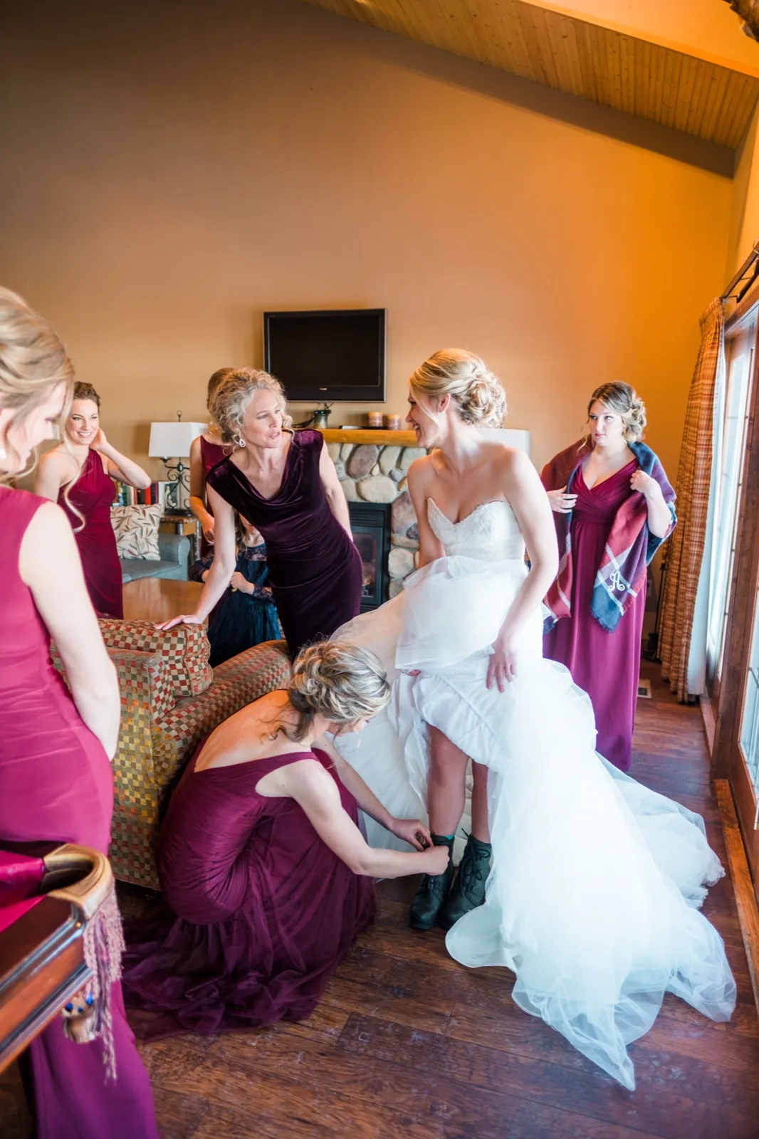 Morgan smiles with women in burgundy while a friend kneels beside her wedding gown