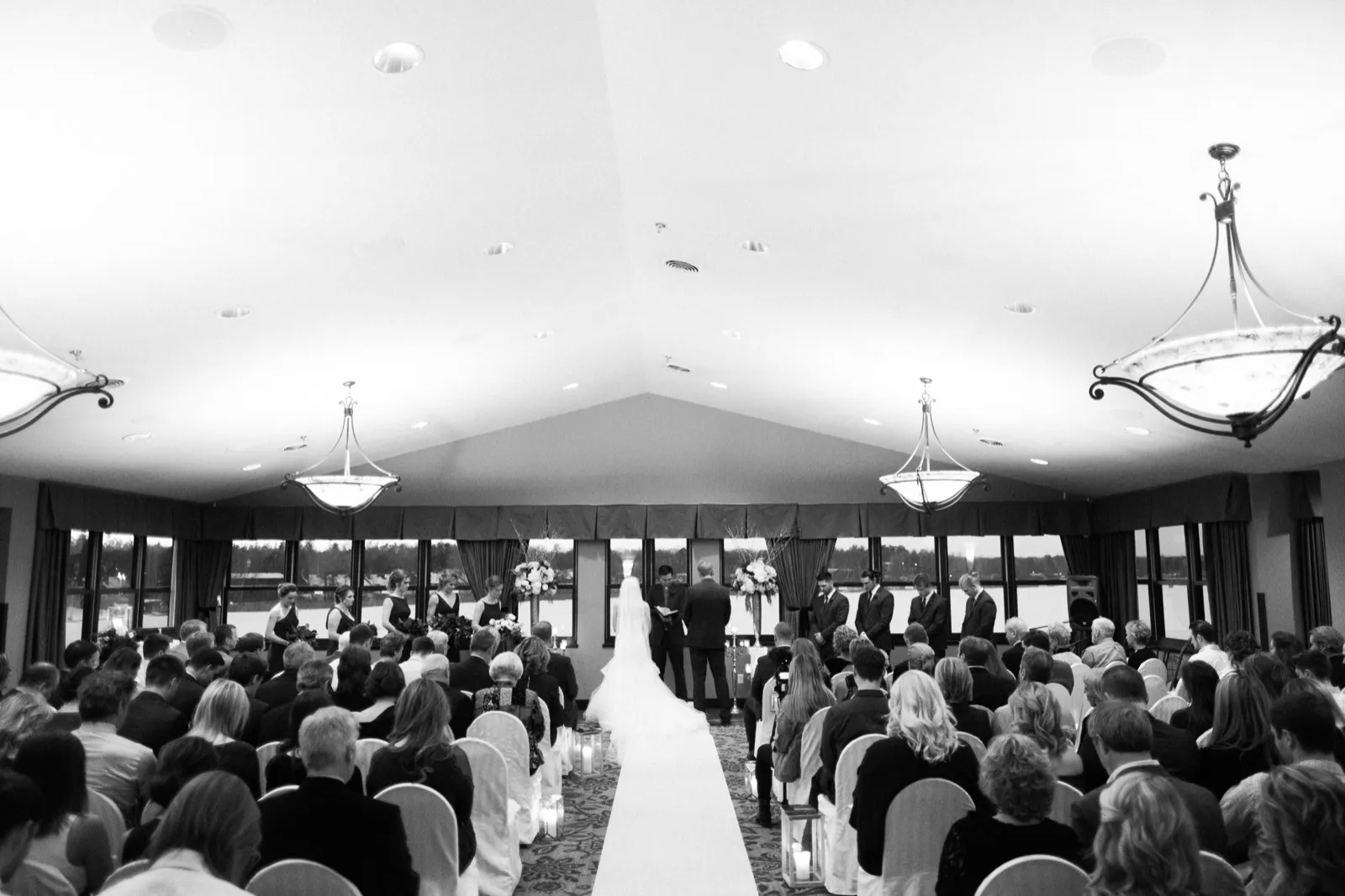 A wide black-and-white view of Morgan and Cole’s indoor ceremony beneath a vaulted ceiling at Breezy Point Resort.