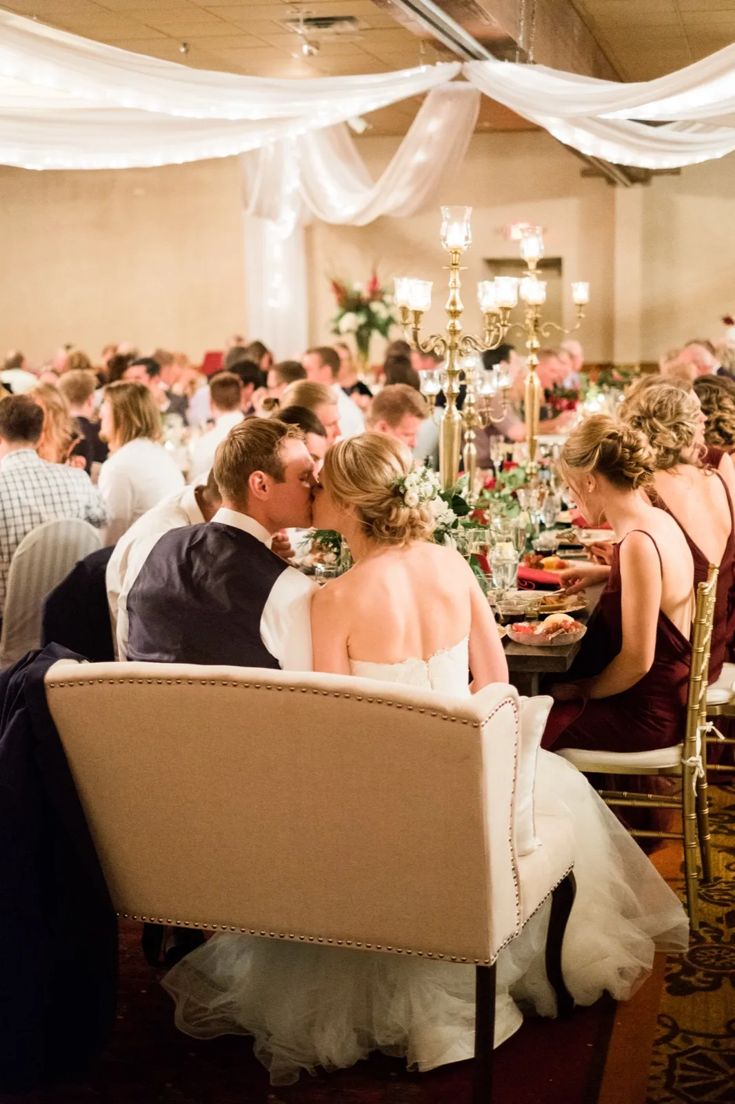 Morgan and Cole kiss at their reception table beneath draped fabric and candlelight at Breezy Point Resort