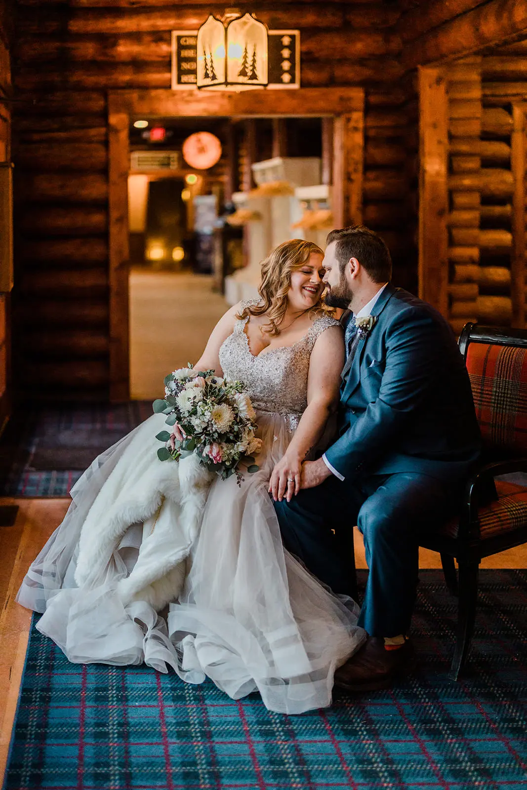 Lauren and Matthew sitting together in the Historic Main Lodge — log walls and plaid carpet — Tim Larsen Photography, Brainerd Lakes MN