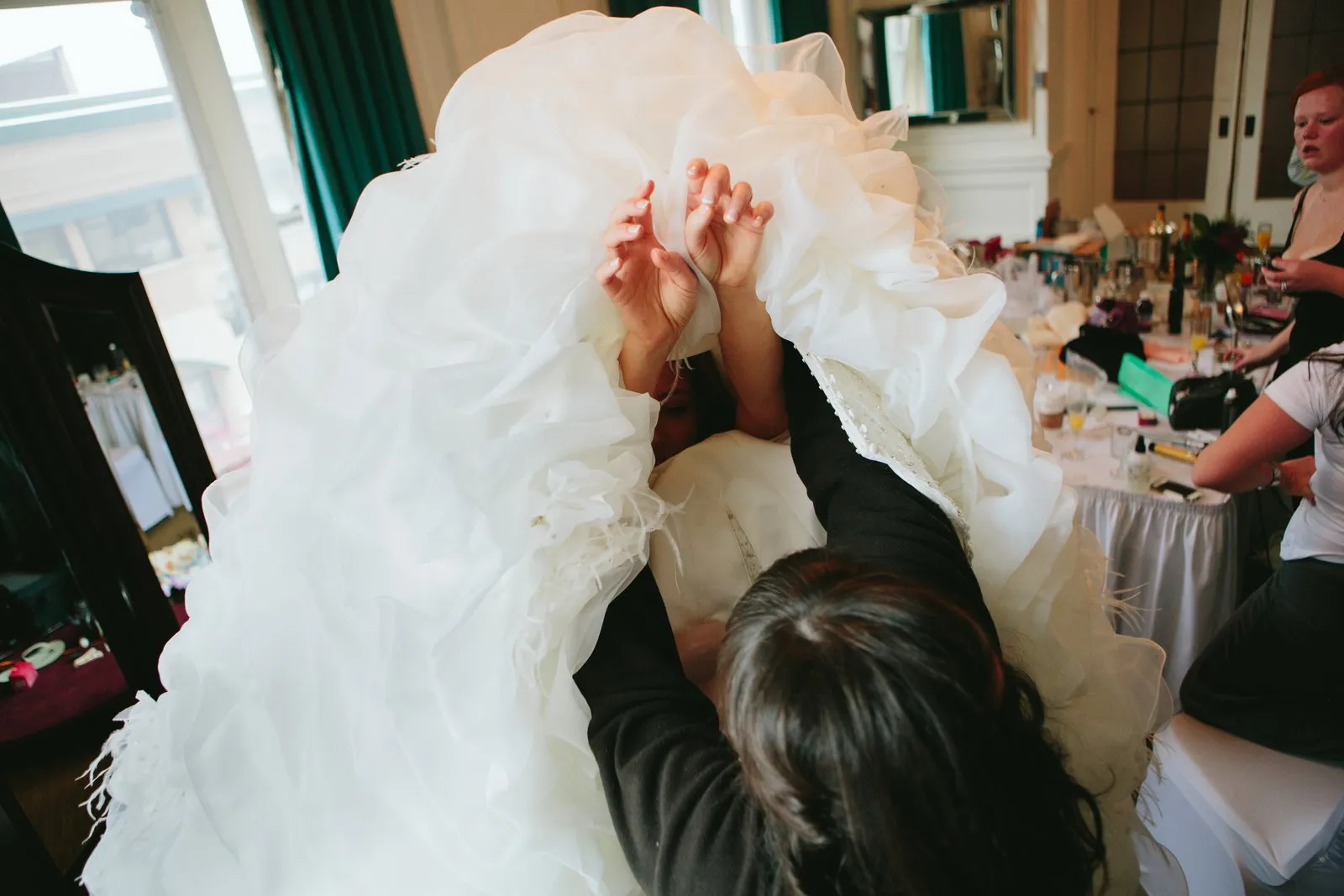Cascading dress lifted overhead as the bride is helped into the gown — getting ready at the Greysolon Plaza — Tim Larsen Photography, Duluth MN
