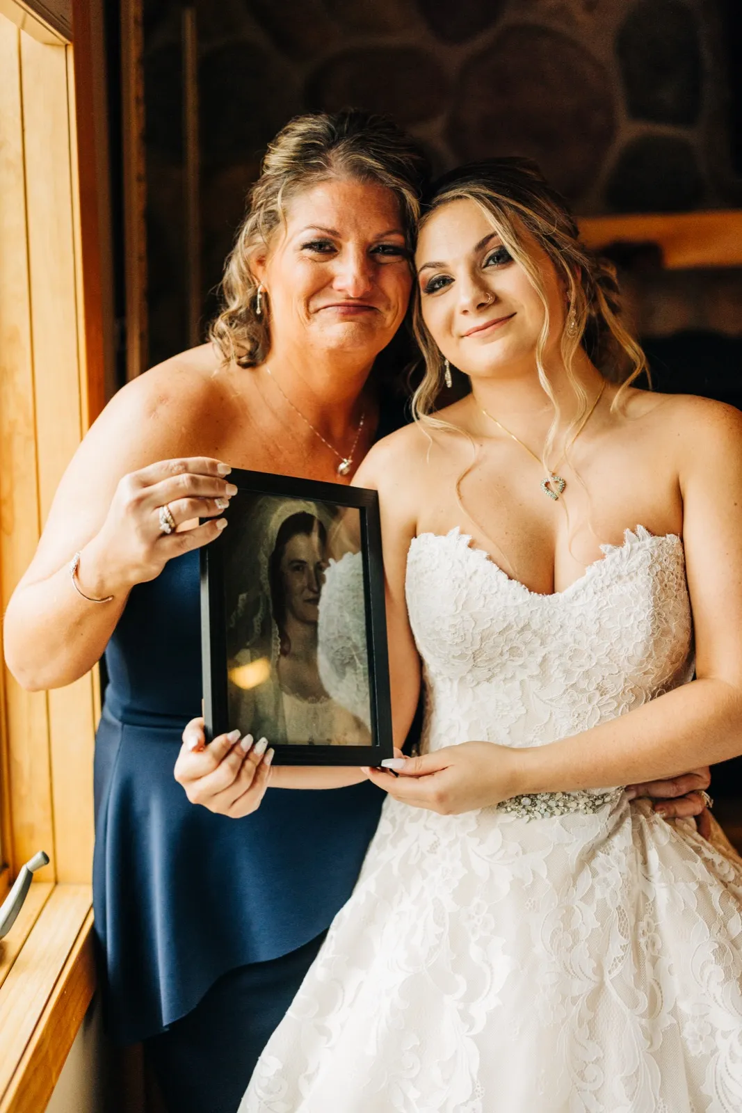 The bride and her mother lean their heads together, holding up a framed antique portrait of a veiled ancestor before the ceremony. — Tim Larsen Photography, Brainerd Lakes MN