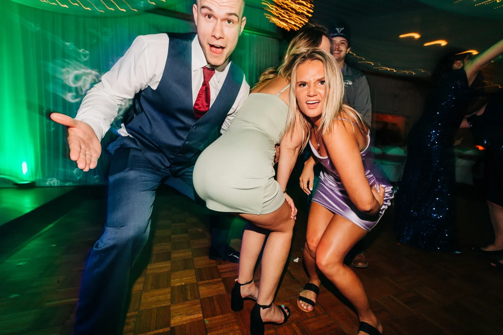 The groom and a guest strike exaggerated dancing poses on a dance floor washed in green light with other guests blurred in motion behind them. — Tim Larsen Photography, Brainerd Lakes MN