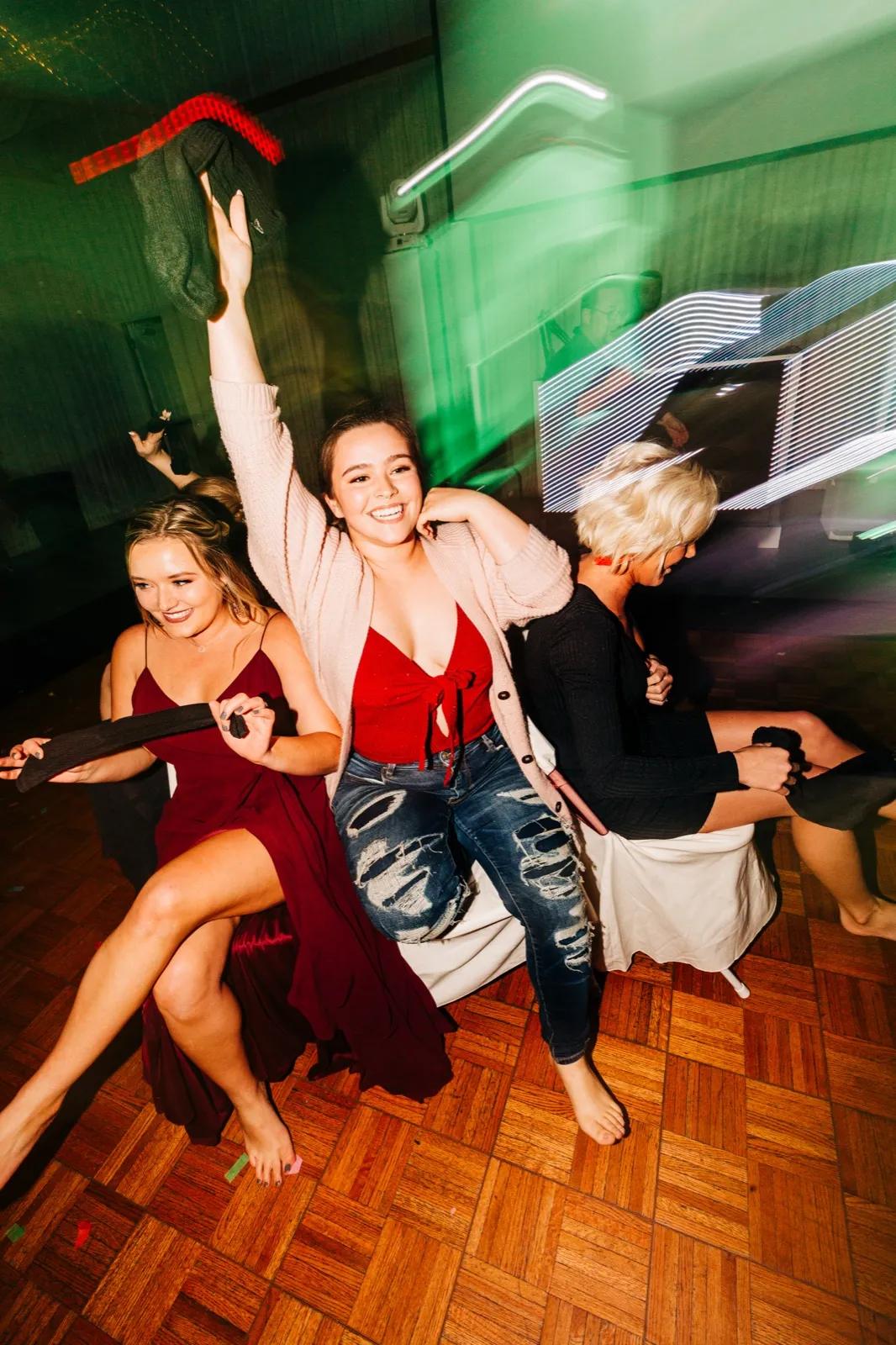 Three women cheer and dance on a parquet floor while colorful light trails streak across the frame from a dragged-shutter flash exposure. — Tim Larsen Photography, Brainerd Lakes MN
