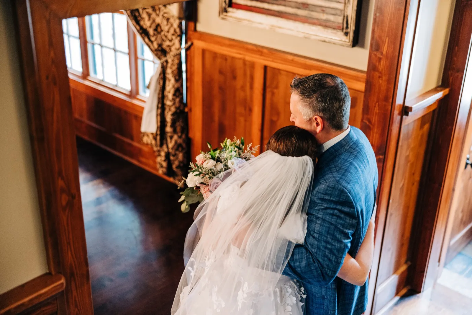 The bride and groom embrace inside a house doorway, photographed from above, with her veil flowing down her back over her bouquet. — Tim Larsen Photography, Brainerd Lakes MN
