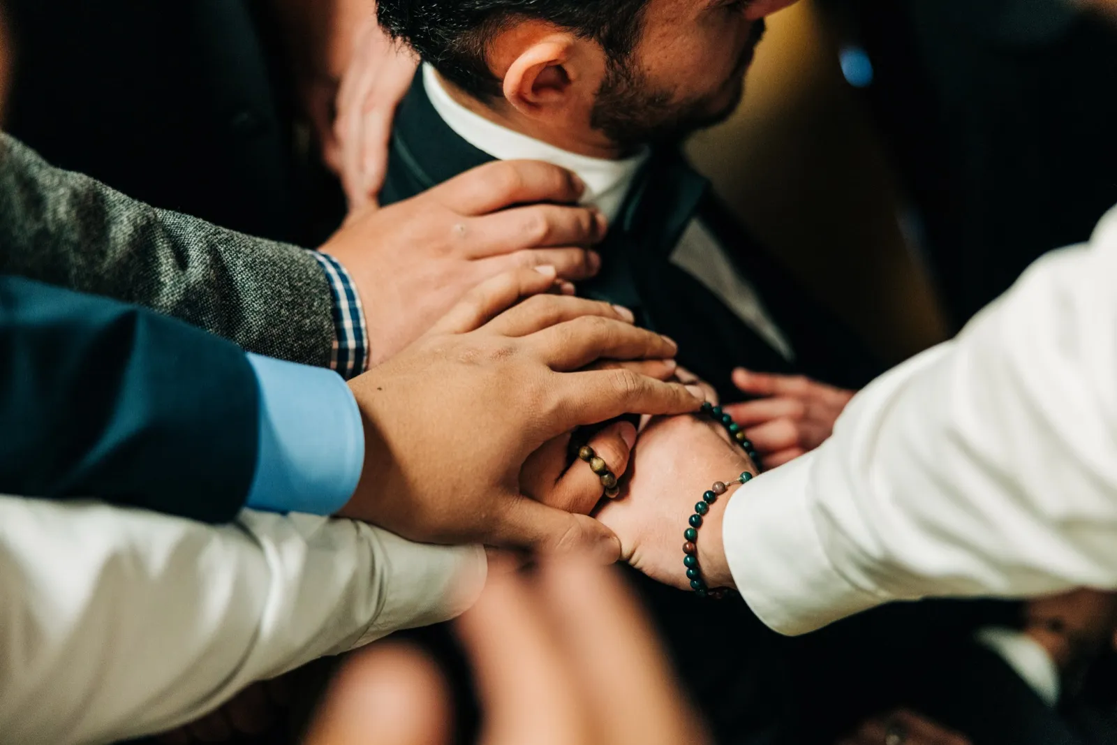 Multiple hands of groomsmen reach in to help adjust the groom's tie and collar before the ceremony. — Tim Larsen Photography, Brainerd Lakes MN