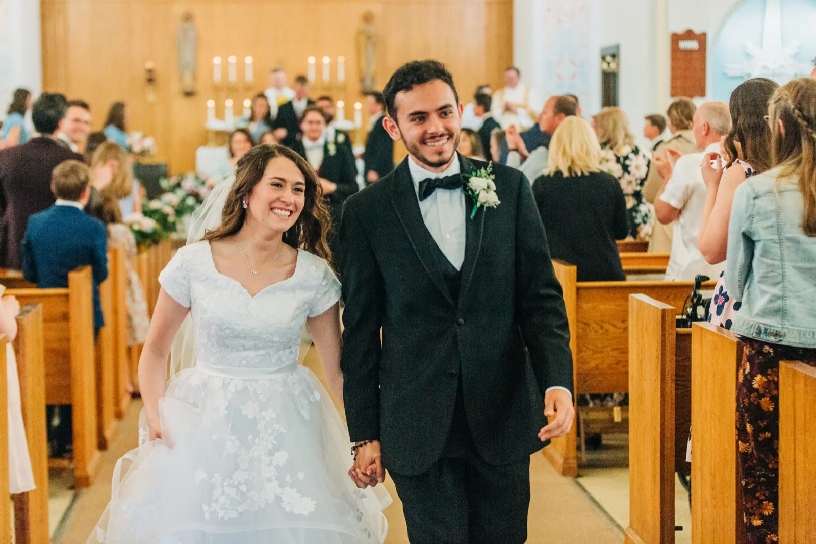 The bride and groom hold hands and beam as they walk back up the church aisle past applauding guests immediately after their ceremony. — Tim Larsen Photography, Brainerd Lakes MN