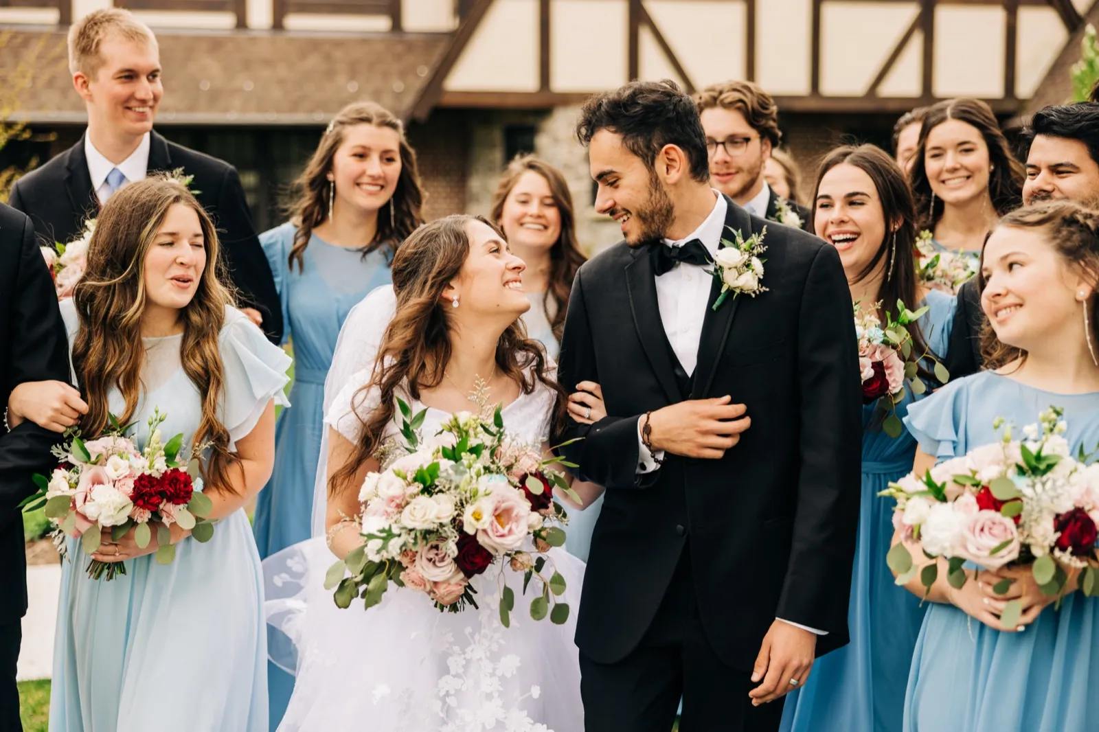 The bride and groom laugh together while their bridal party in dusty blue dresses and dark suits reacts with laughter around them. — Tim Larsen Photography, Brainerd Lakes MN