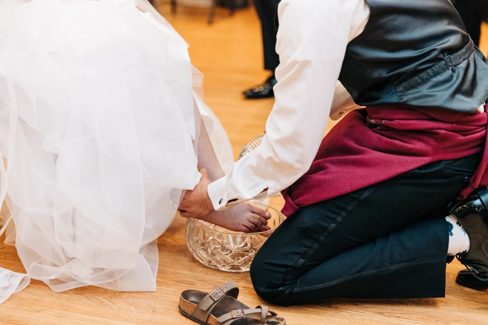 The groom kneels on a wood floor and washes the bride's bare foot in a crystal bowl beside her discarded sandals. — Tim Larsen Photography, Brainerd Lakes MN