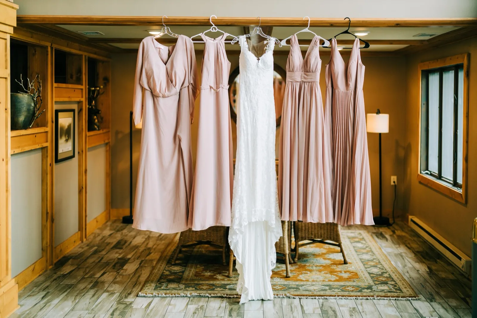 Shannon's gown hangs between five blush bridesmaid dresses on a wooden beam in a warmly lit lodge room at Madden's — Tim Larsen Photography, Brainerd Lakes MN