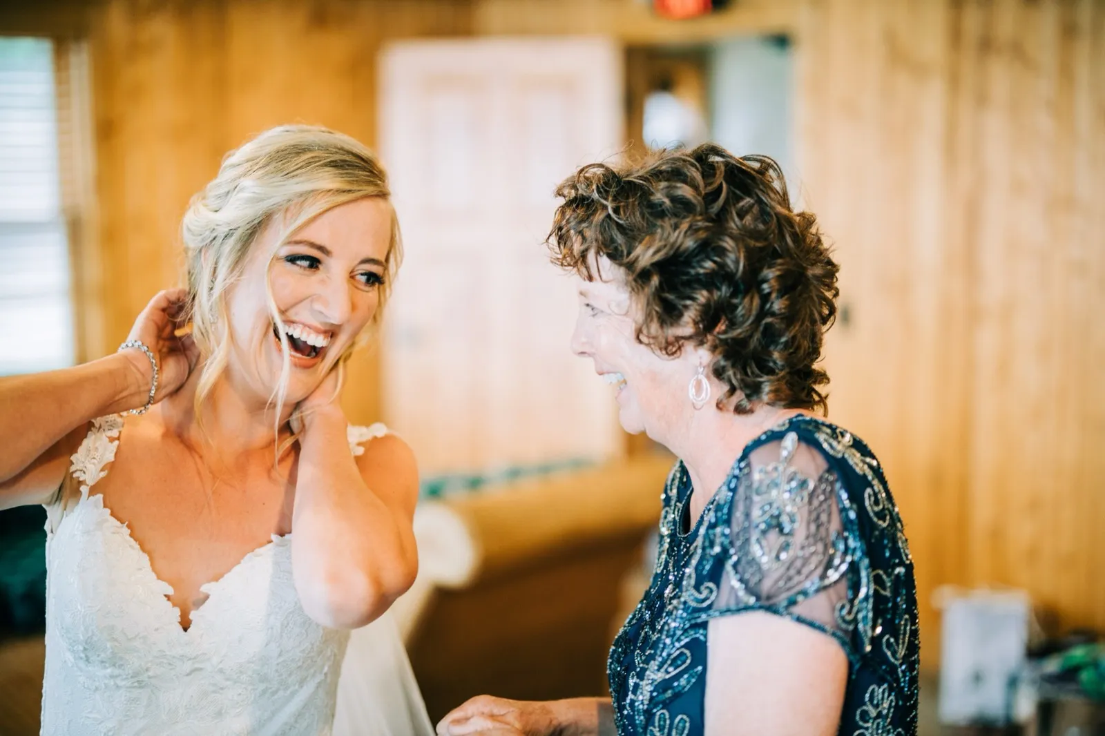 Shannon laughs with her mother, in a beaded navy dress, in the pine-paneled getting-ready room — Tim Larsen Photography, Brainerd Lakes MN