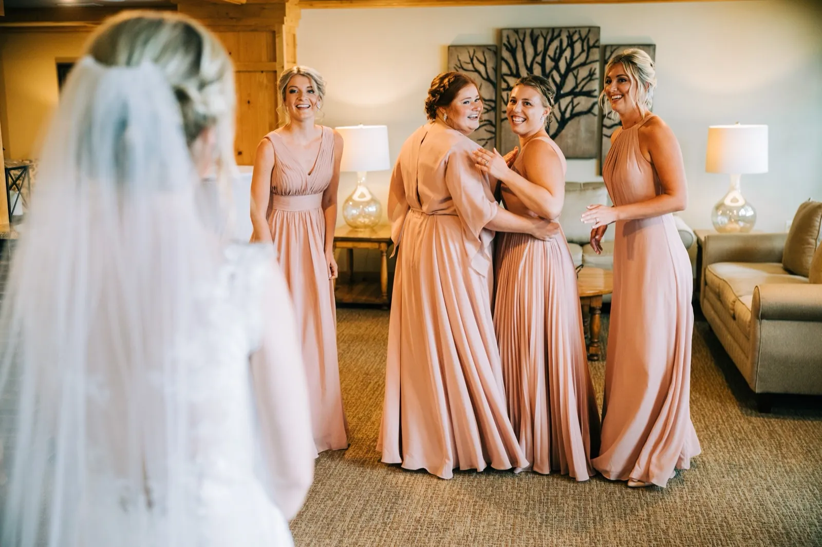 Four bridesmaids in blush gowns react with delight as Shannon reveals her dress and veil in a warmly lit suite at Madden's — Tim Larsen Photography, Brainerd Lakes MN