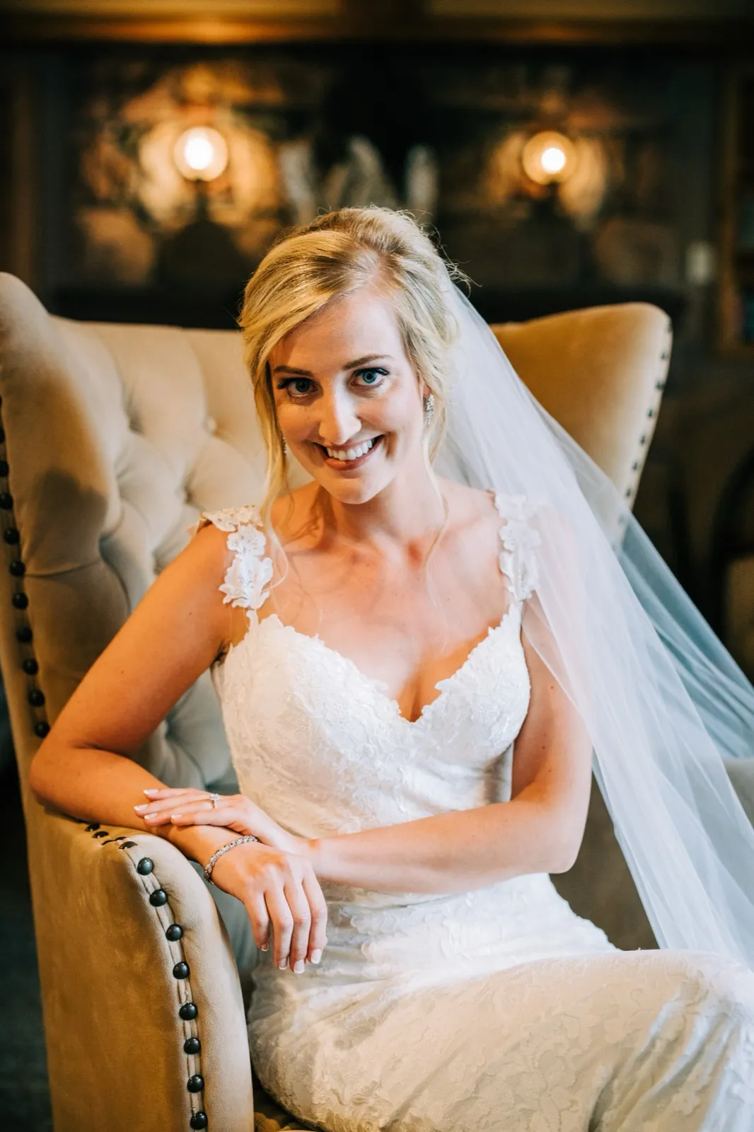 Shannon smiles in her lace gown from a tufted velvet chair, her veil draped over the arm — Tim Larsen Photography, Brainerd Lakes MN