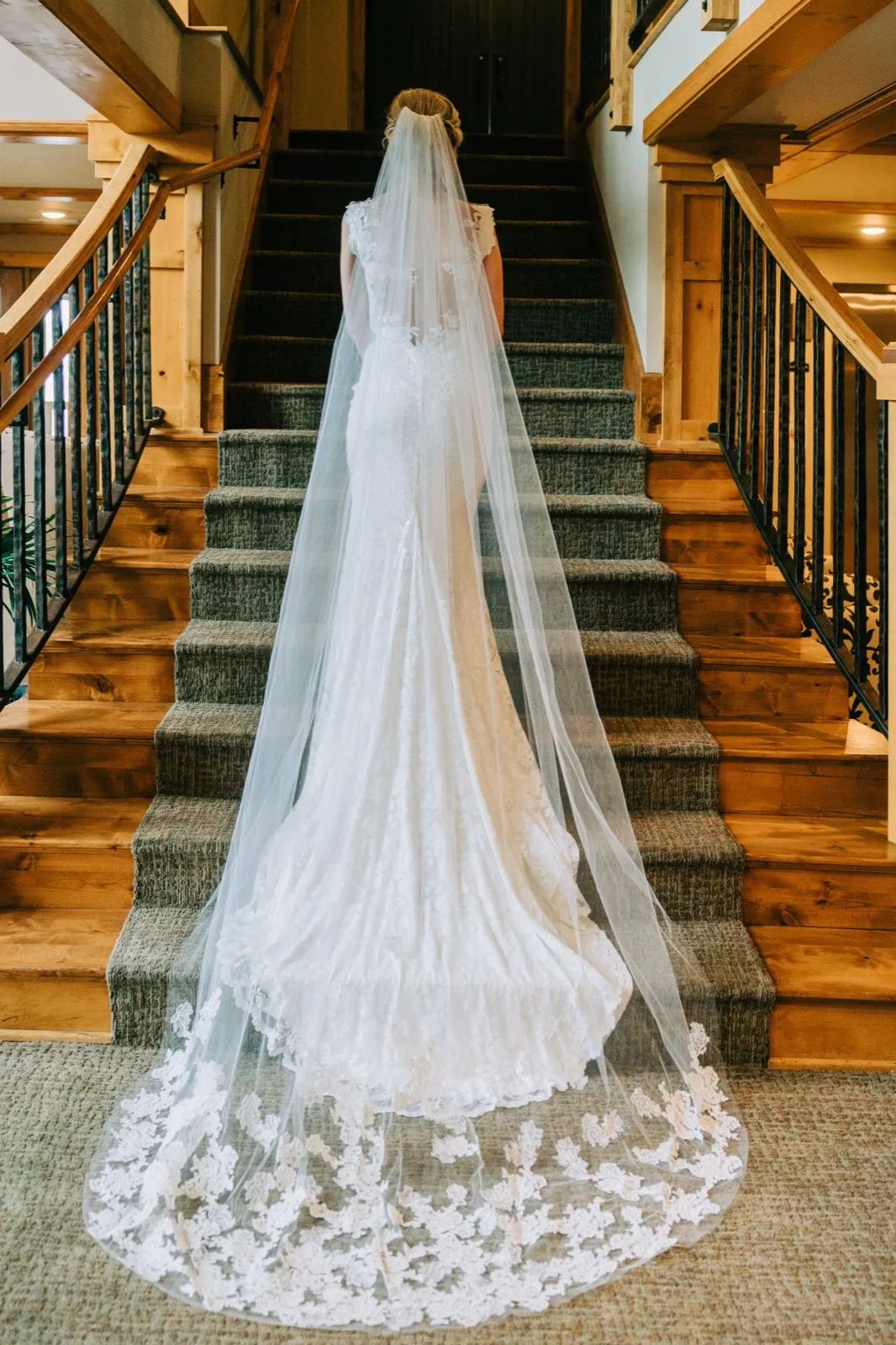 Shannon at the base of a wooden staircase, her lace-trimmed veil and train cascading several steps behind her — Tim Larsen Photography, Brainerd Lakes MN