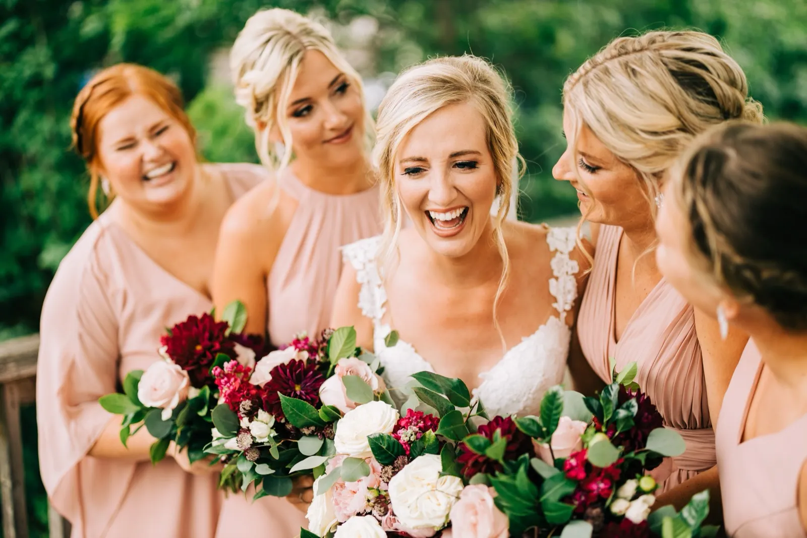 Shannon laughs with her mouth wide open as her bridesmaids gather close, all holding burgundy and blush bouquets — Tim Larsen Photography, Brainerd Lakes MN