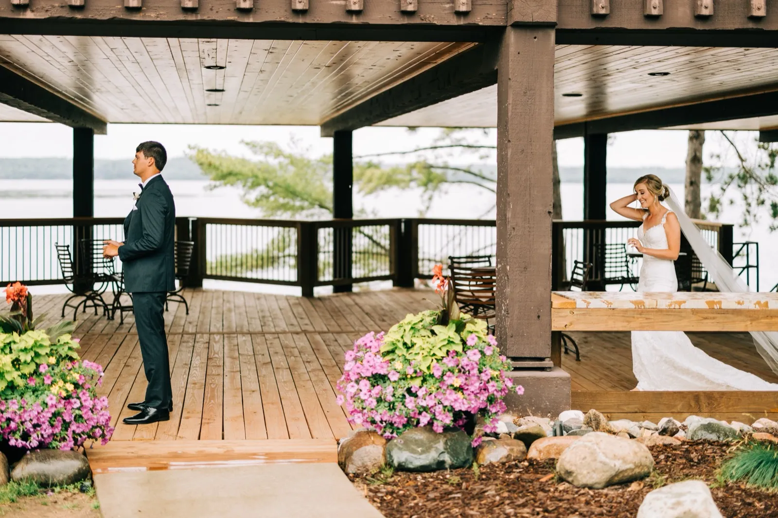 Zach waits at one end of the covered lakeside pavilion while Shannon adjusts her veil at the other, Gull Lake visible behind them at Madden's — Tim Larsen Photography, Brainerd Lakes MN