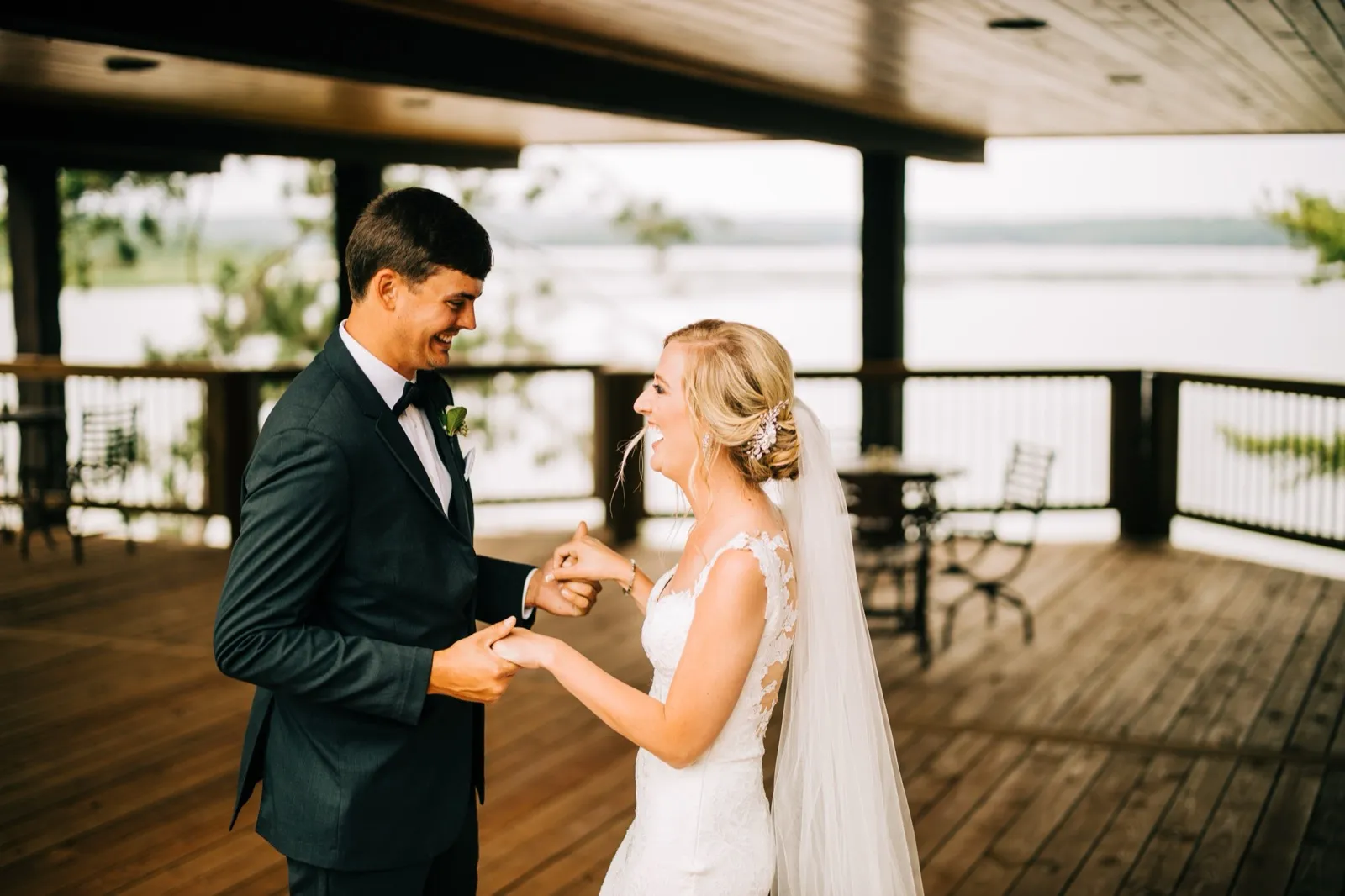 Shannon and Zach hold hands and laugh during their first look on a covered porch overlooking Gull Lake at Madden's — Tim Larsen Photography, Brainerd Lakes MN