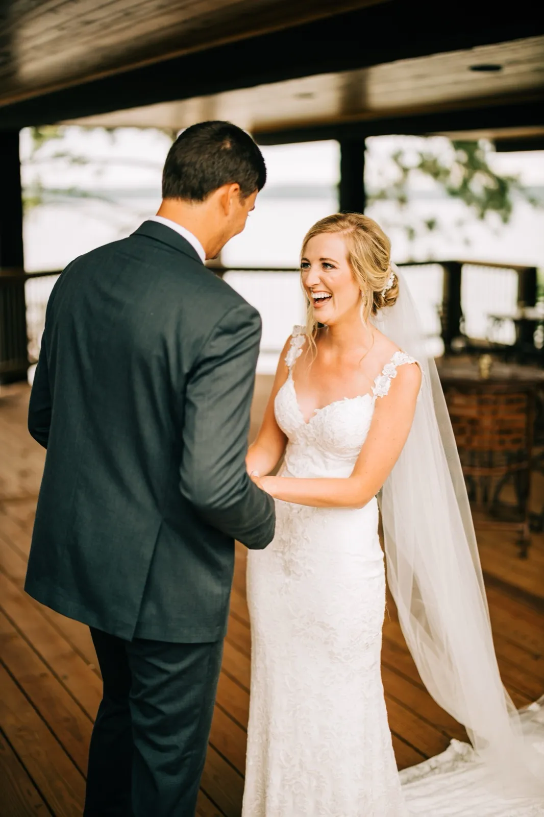 Shannon laughs as she holds Zach's arms during their first look on the covered lakeside porch — Tim Larsen Photography, Brainerd Lakes MN