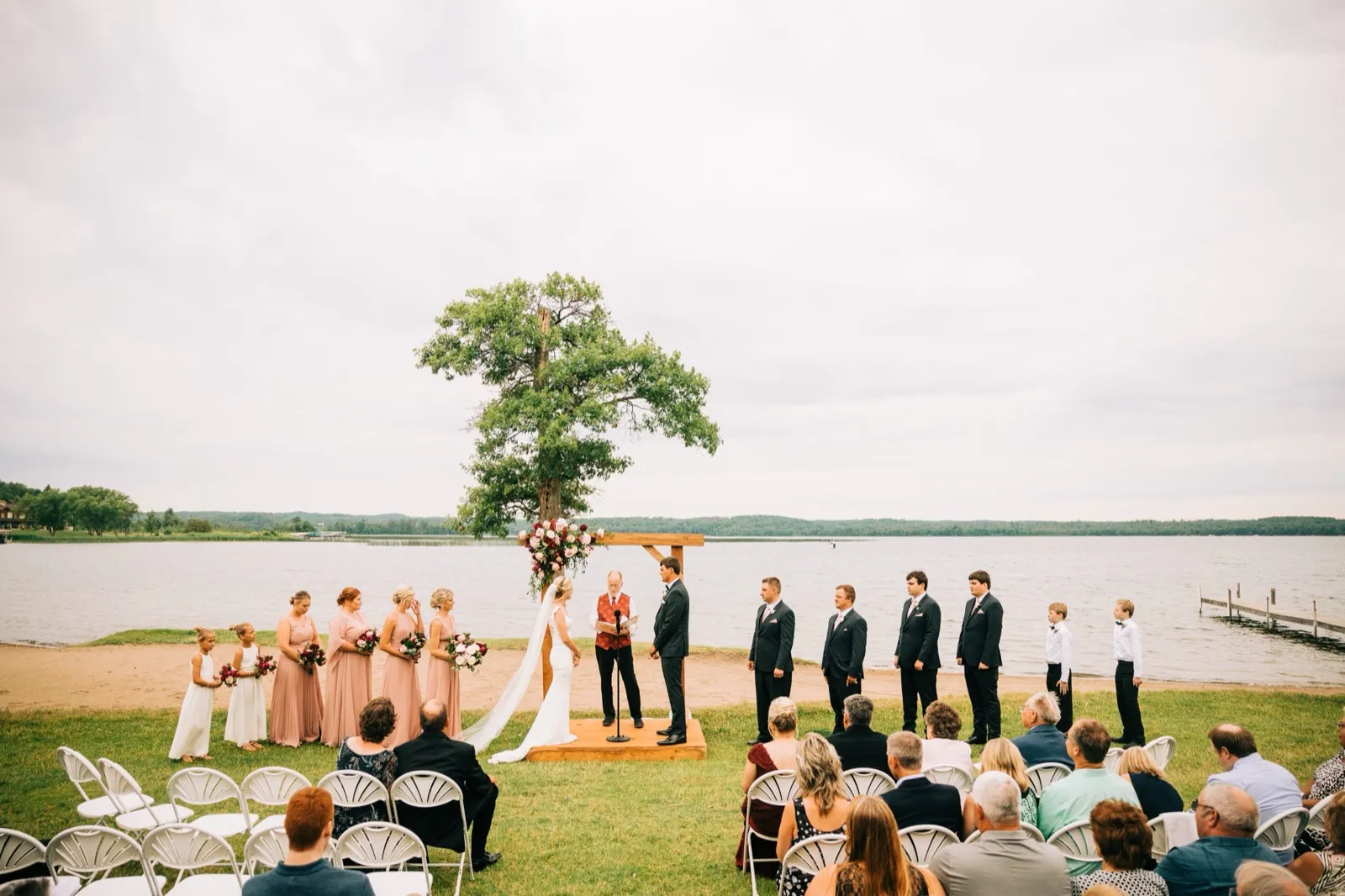 A wide view of the lakeside ceremony at Madden's — the couple and bridal party beneath a floral arch with Gull Lake behind — Tim Larsen Photography, Brainerd Lakes MN