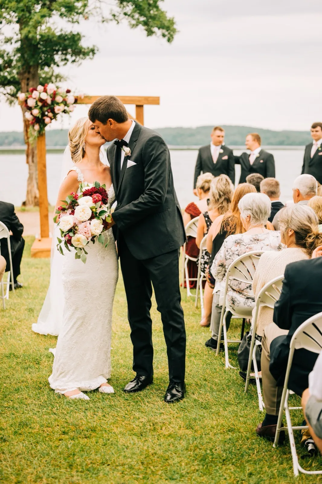 Shannon and Zach kiss in the aisle after their ceremony as seated guests look on, Gull Lake and the floral arch behind them — Tim Larsen Photography, Brainerd Lakes MN