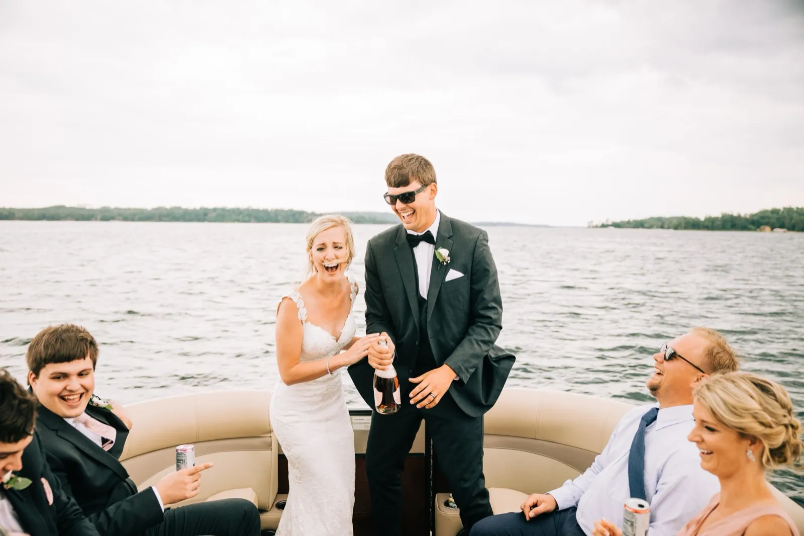Shannon laughs as Zach uncorks champagne on a pontoon boat surrounded by their bridal party out on Gull Lake at Madden's — Tim Larsen Photography, Brainerd Lakes MN
