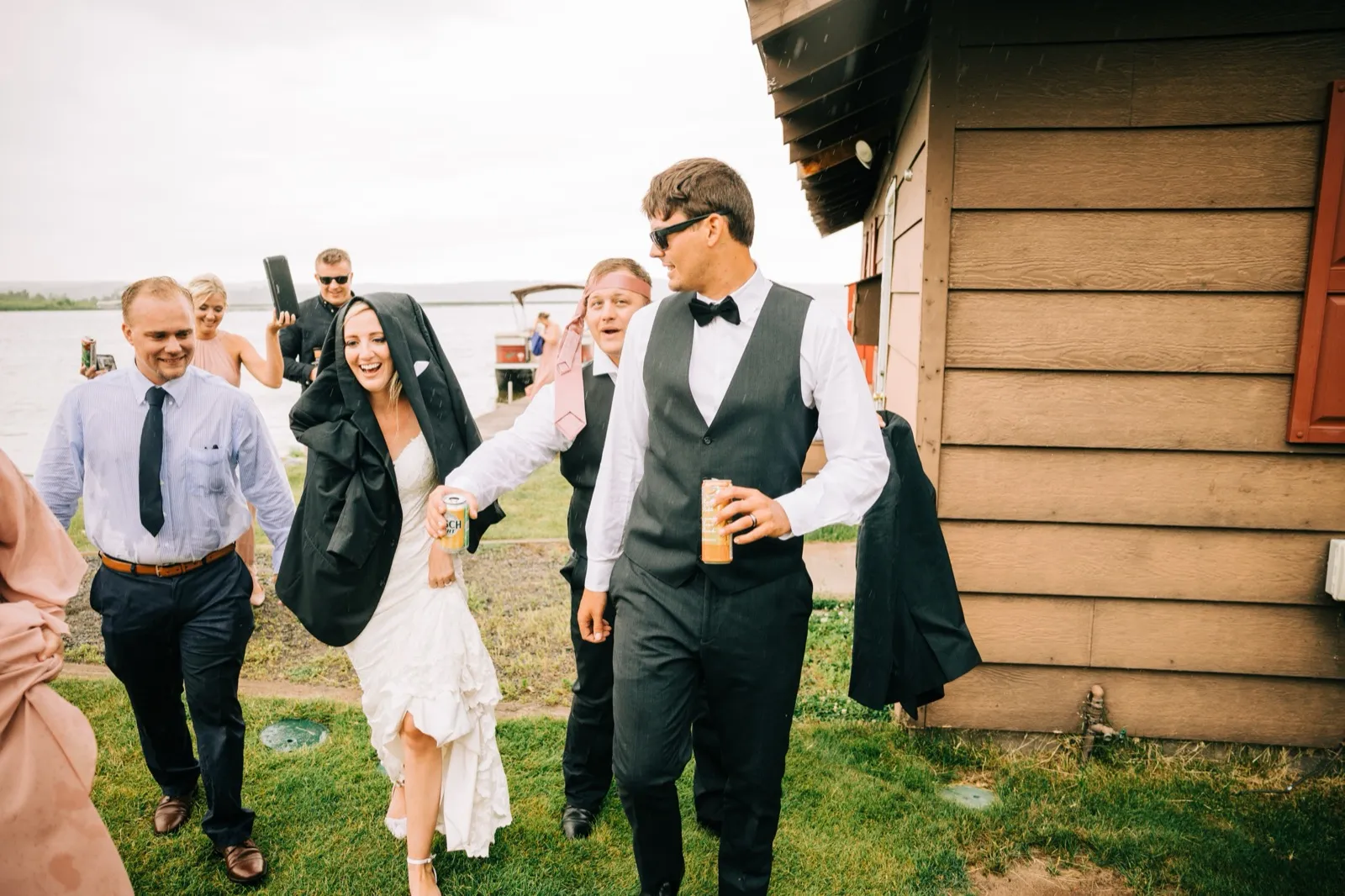 Shannon walks across the grass laughing, drink in hand, as Zach carries his jacket beside her during a passing shower at Madden's — Tim Larsen Photography, Brainerd Lakes MN