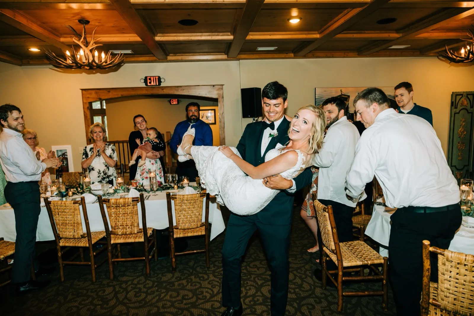 Zach carries a laughing Shannon into the reception beneath the antler chandeliers and exposed beams at Madden's — Tim Larsen Photography, Brainerd Lakes MN