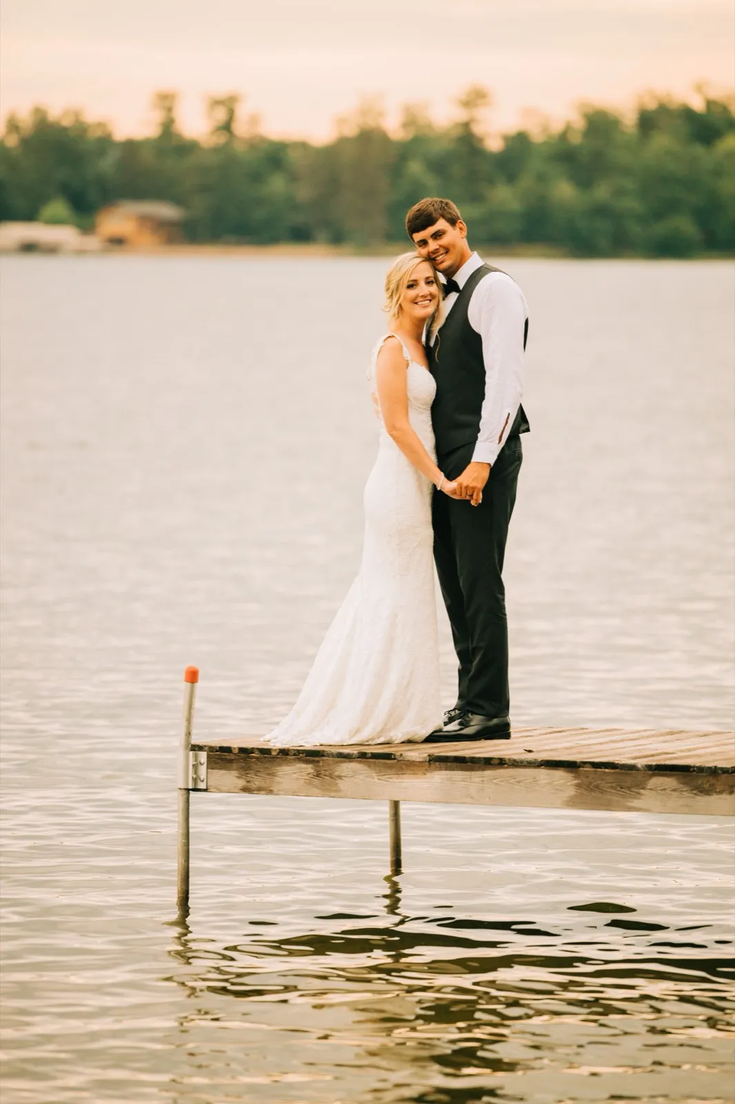 Shannon and Zach hold hands at the end of the dock, warm evening light spreading across the water at Madden's on Gull Lake — Tim Larsen Photography, Brainerd Lakes MN