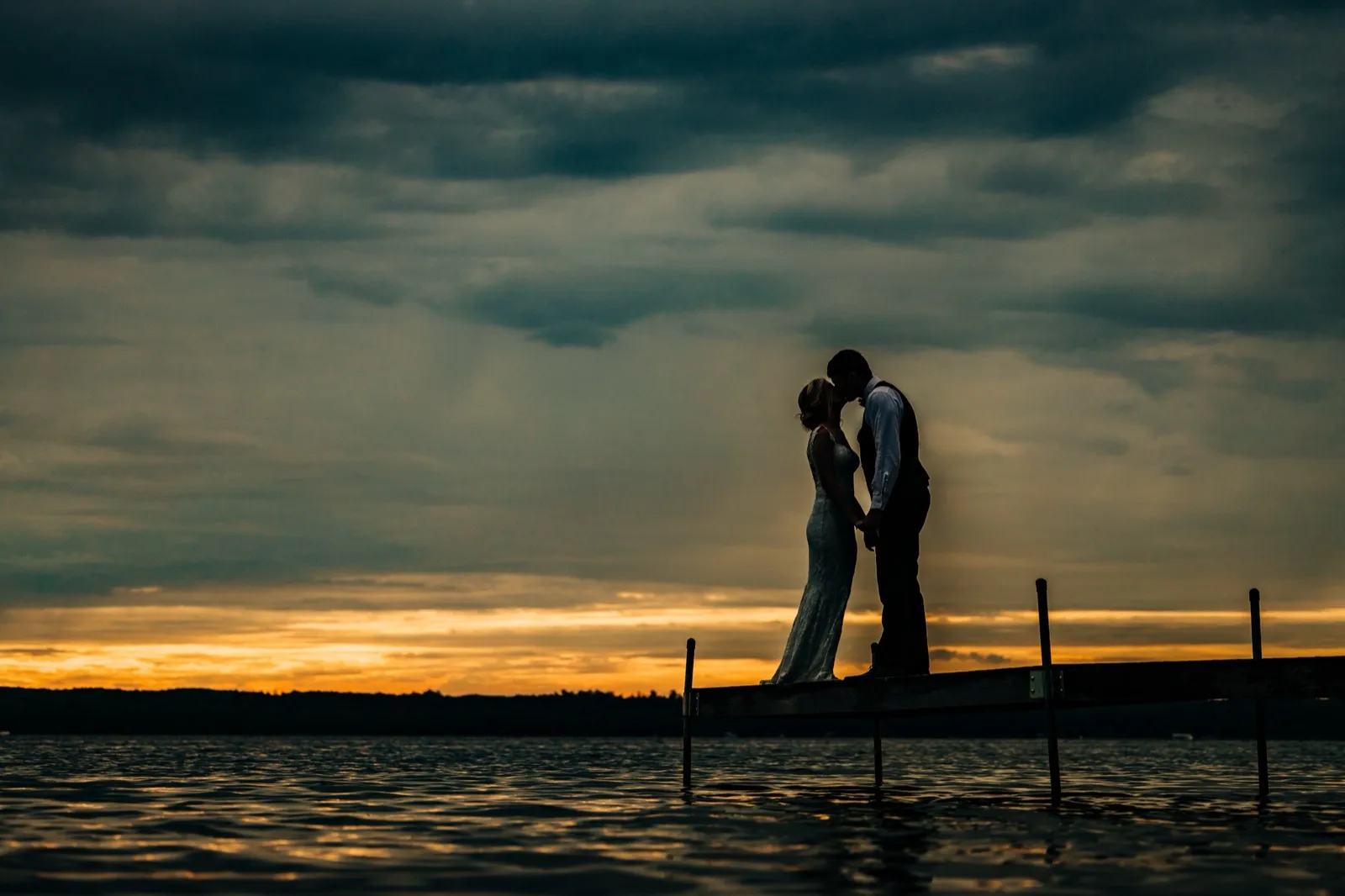 Shannon and Zach kiss in silhouette at the end of the dock beneath a dramatic teal-and-orange dusk sky over Gull Lake — Tim Larsen Photography, Brainerd Lakes MN