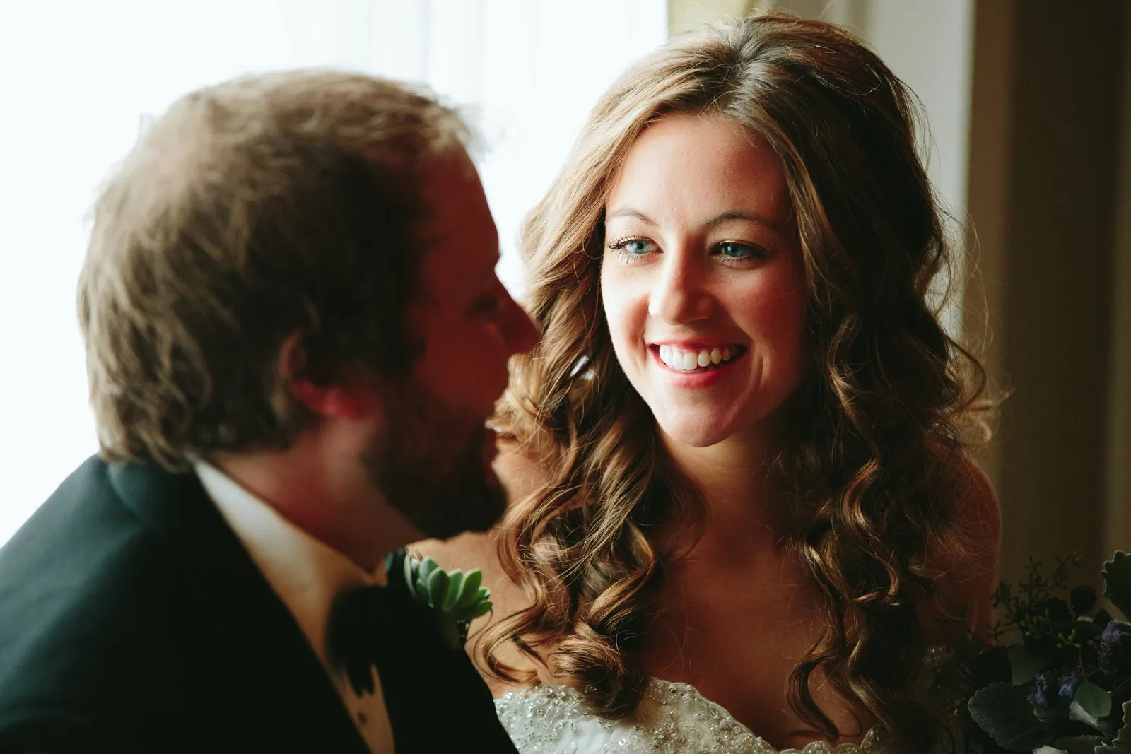 Bride's radiant smile in sharp focus with the soft-focus groom framing the foreground, both bathed in window light — Greysolon Plaza — Tim Larsen Photography, Duluth MN
