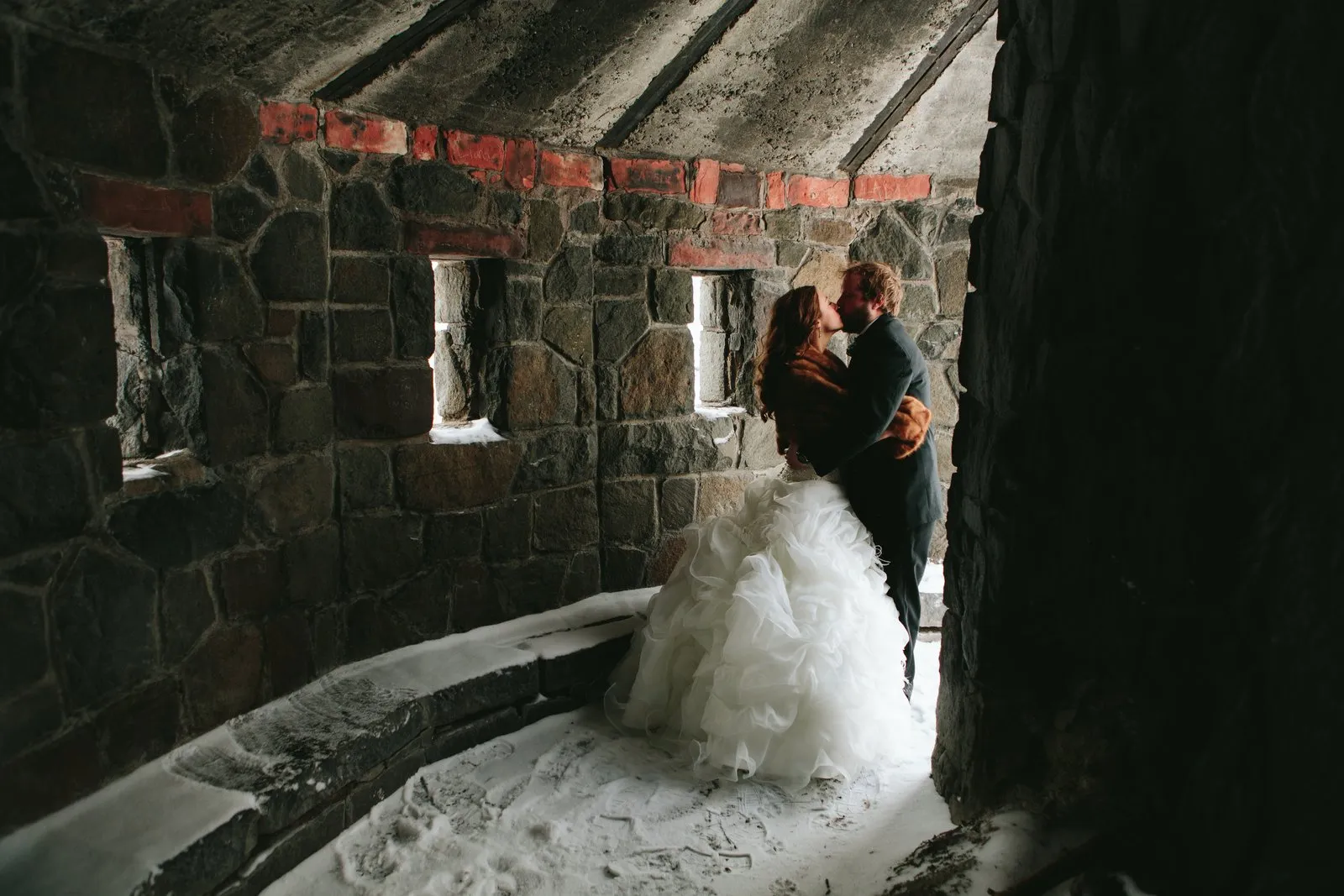Couple sharing a kiss in a stone-walled alcove with snow drifted across the floor — Duluth winter wedding portrait — Tim Larsen Photography, Duluth MN