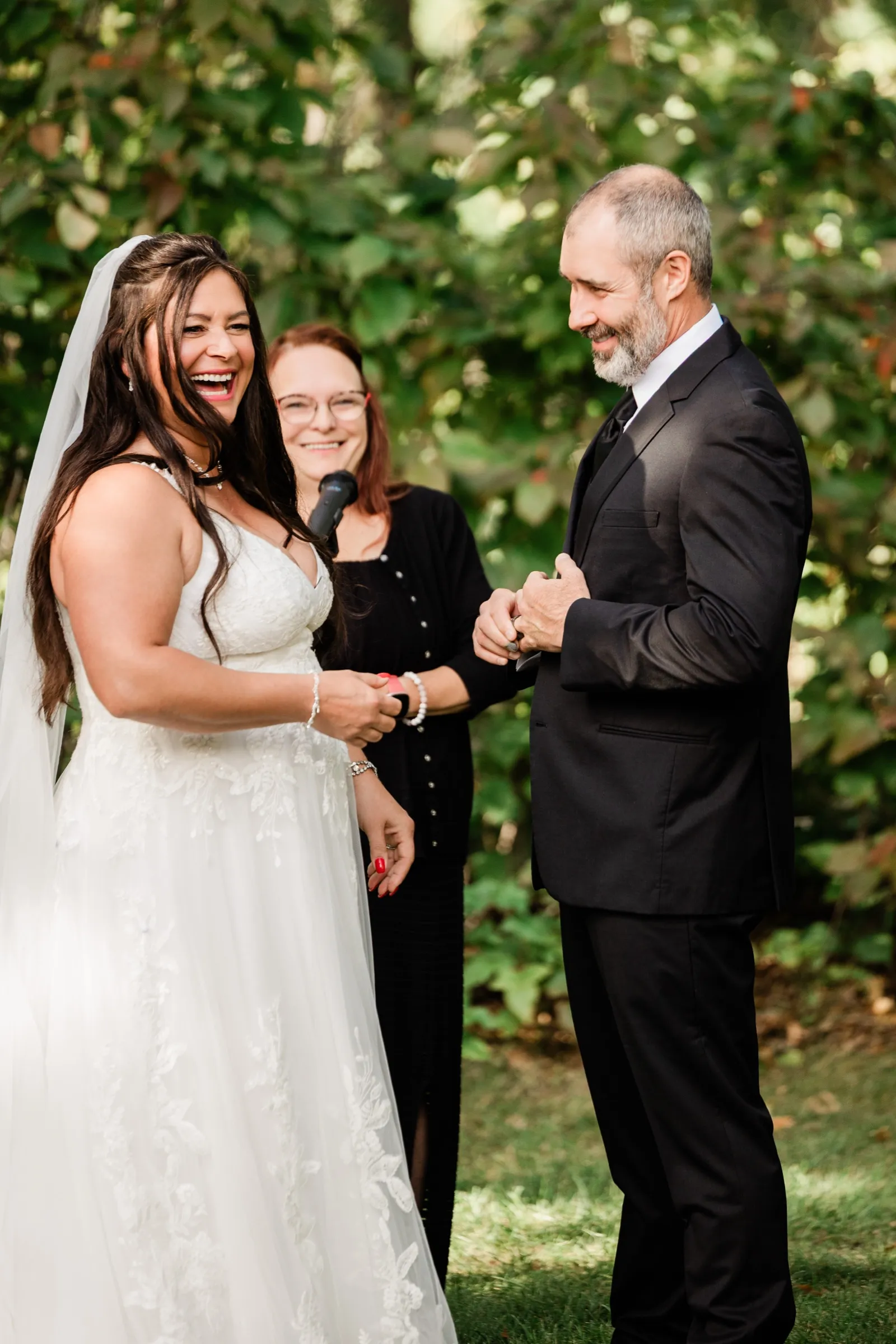 Amber bursts out laughing during the ring exchange while Don grins and the officiant smiles between them. — Tim Larsen Photography, Brainerd Lakes MN