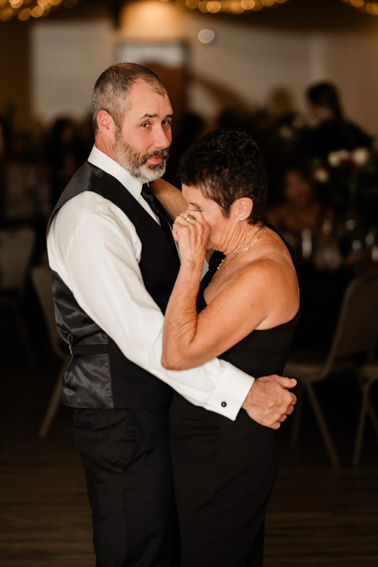 Don dances with a short-haired woman in a black dress who wipes her eyes with her hand while he looks toward the camera. — Tim Larsen Photography, Brainerd Lakes MN