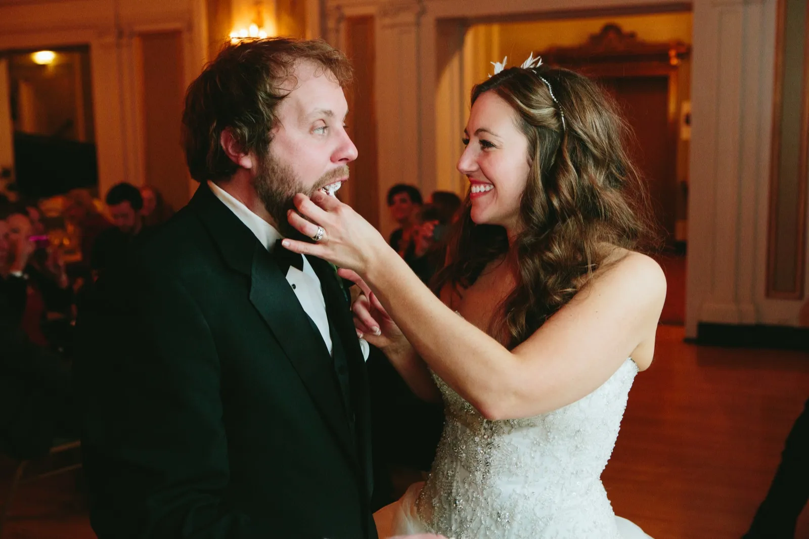 Bride feeding the groom cake in a warm tungsten-lit two-shot, her hand framing his reaction — Greysolon Ballroom cake cutting — Tim Larsen Photography, Duluth MN