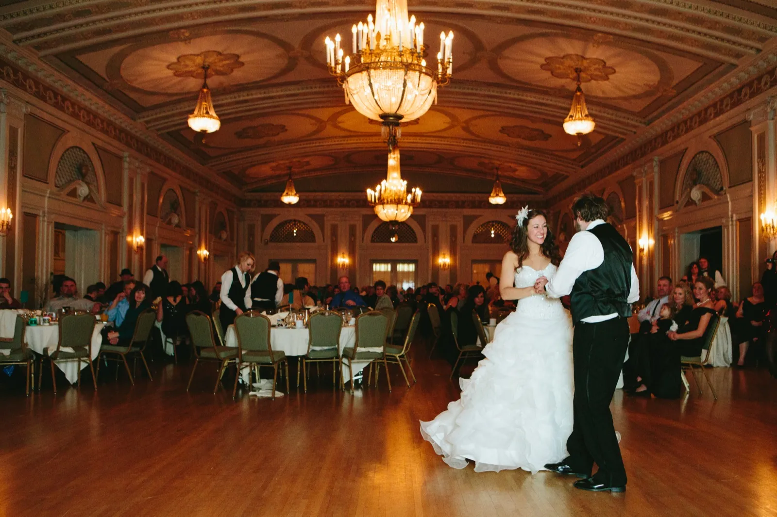 Wide environmental first dance — the ornate Greysolon Ballroom ceiling and chandeliers dominate, the couple anchoring the dance floor below — Tim Larsen Photography, Duluth MN