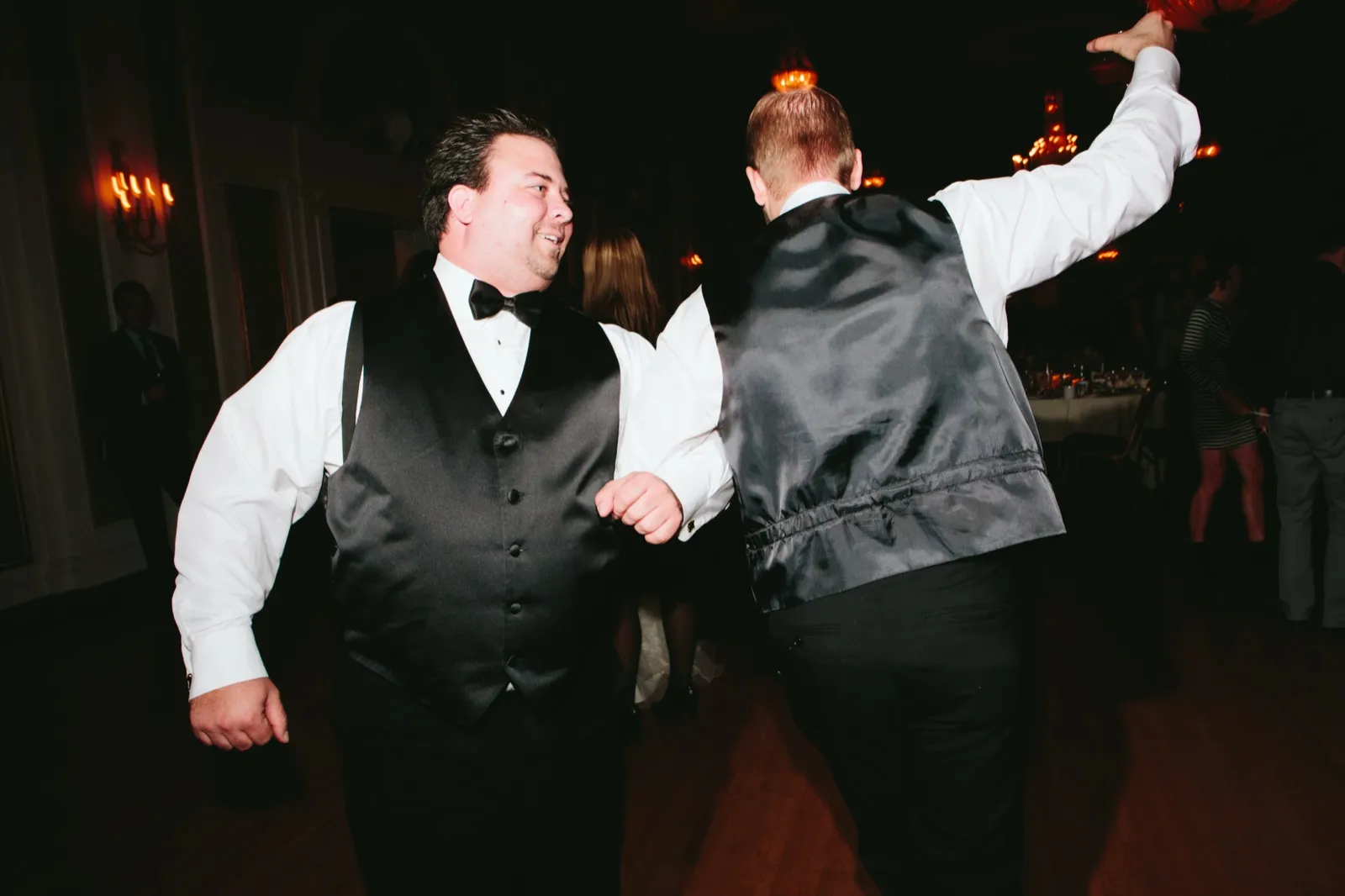 Two groomsmen mid-dance on the Greysolon Ballroom dance floor, one with arm raised mid-celebration — winter wedding party — Tim Larsen Photography, Duluth MN